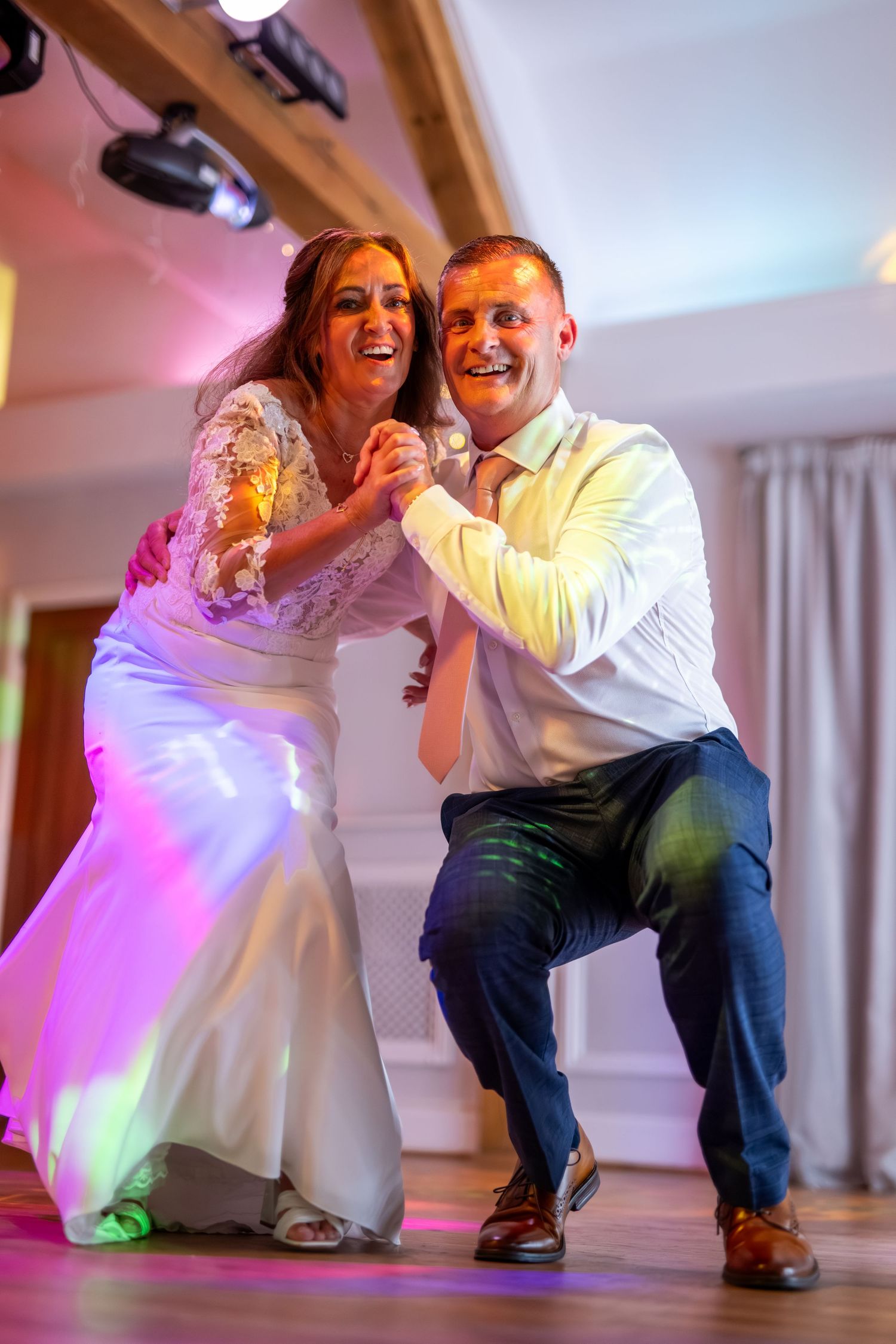 Wedding couple performs dramatic dance moves on reception floor under colorful lighting.