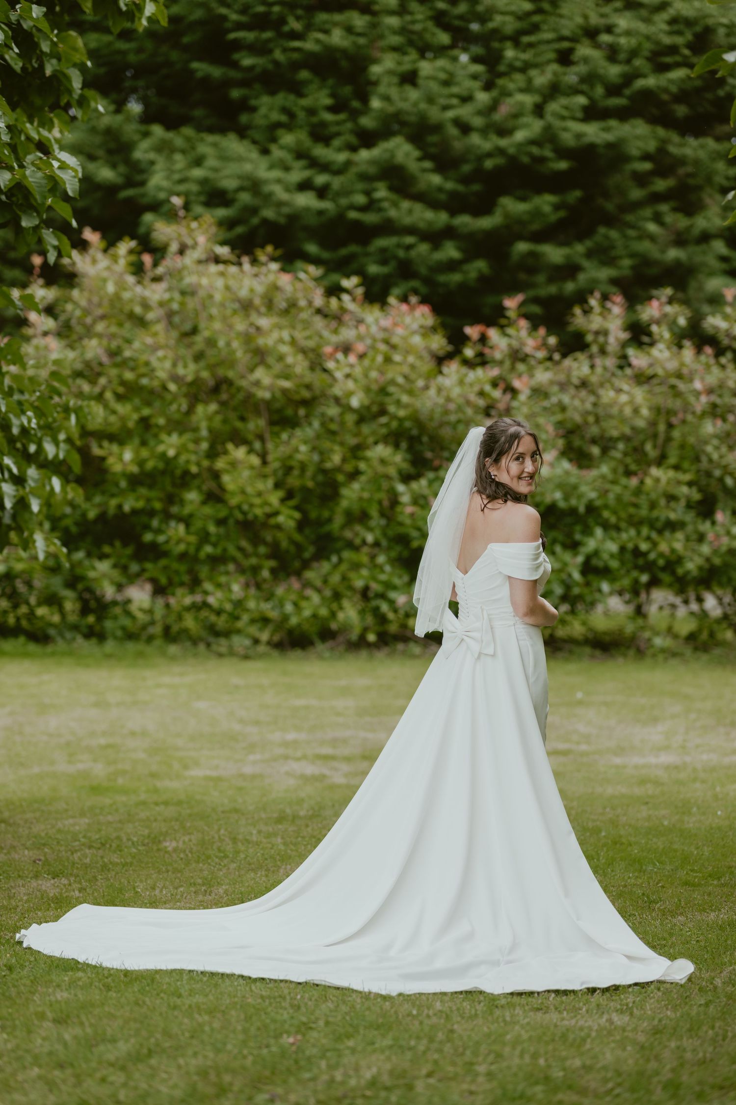 Elegant white wedding dress with a flowing train photographed in a lush garden setting.