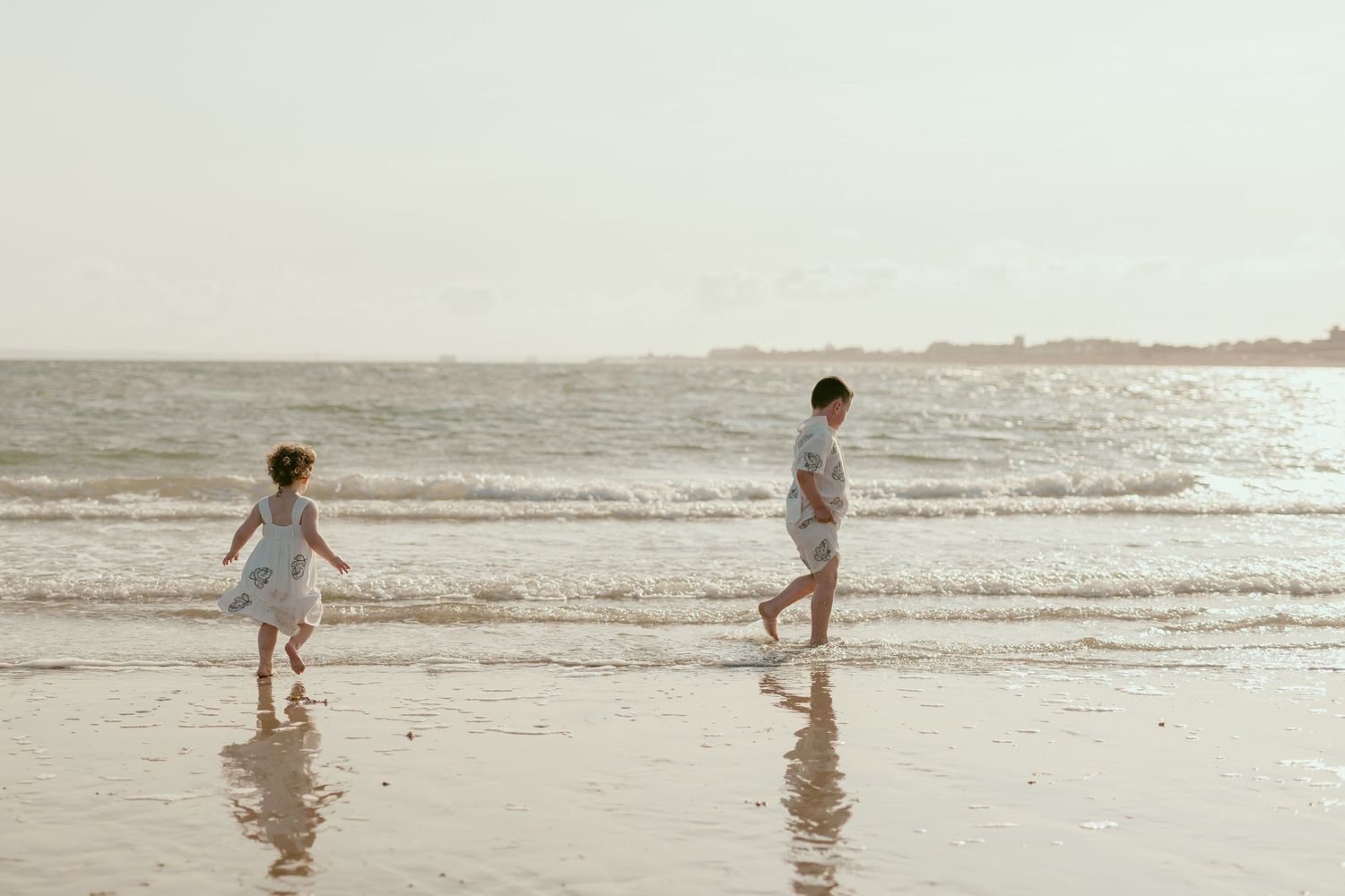 Two people walk along a misty beach shoreline at sunset.