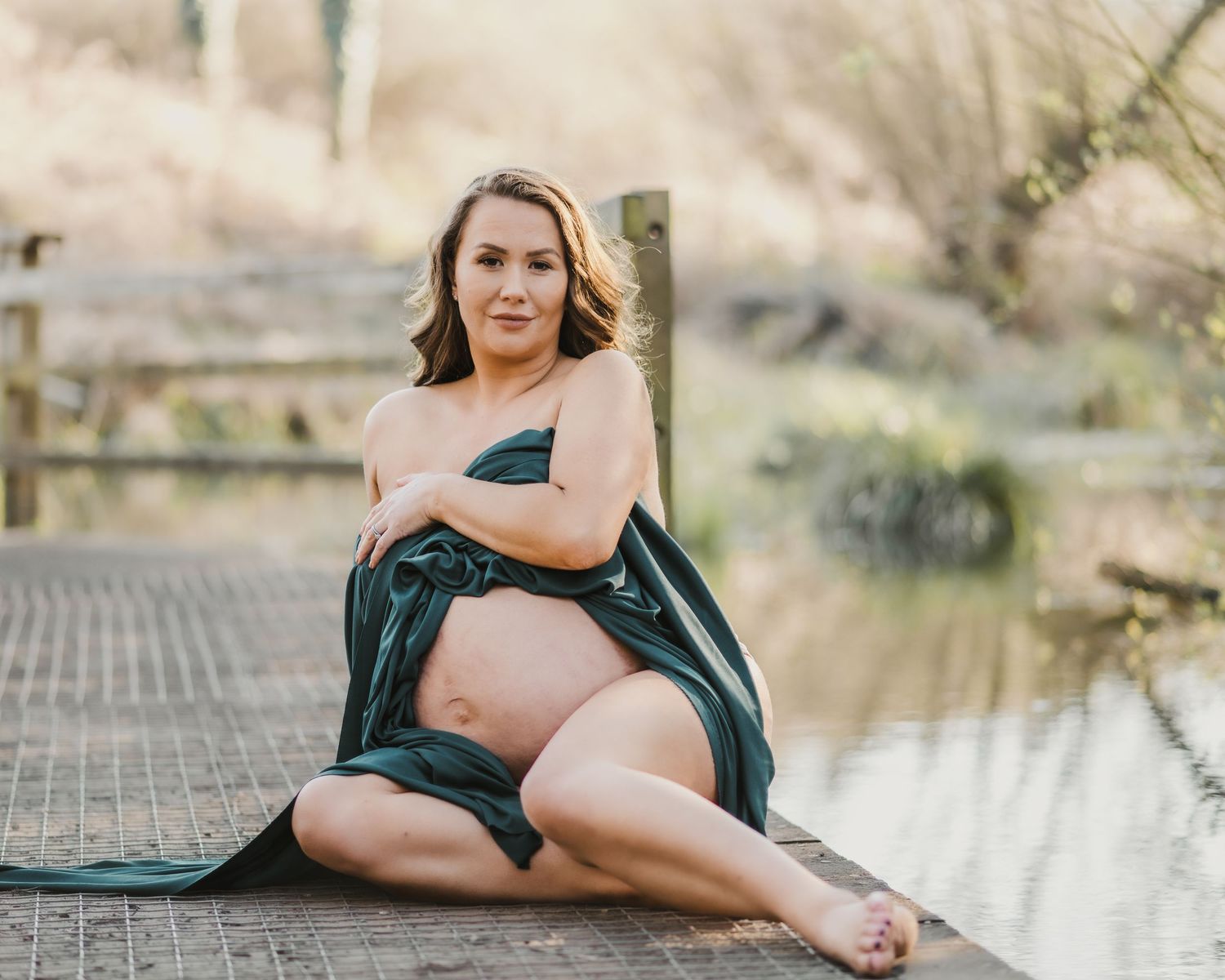 Maternity photoshoot at sunset featuring poses on wooden dock in teal dress.