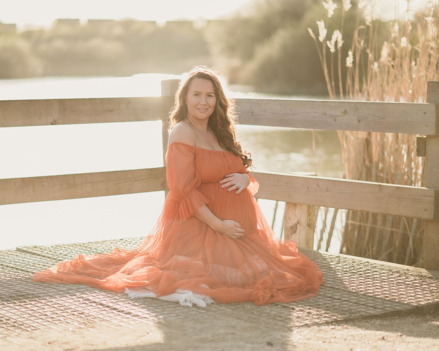 Dreamy maternity photos in coral dress during sunset by waterfront.