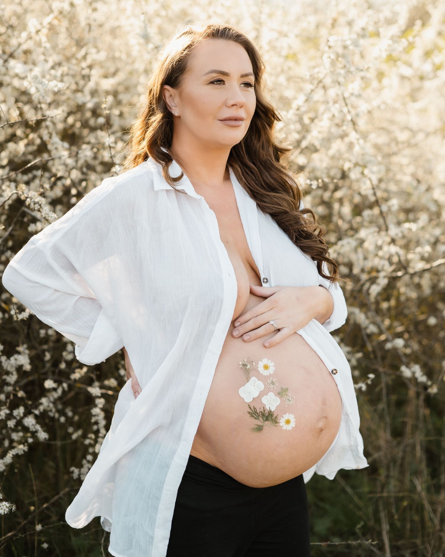 Artistic maternity photo with delicate flowers placed on the belly against a bright background.