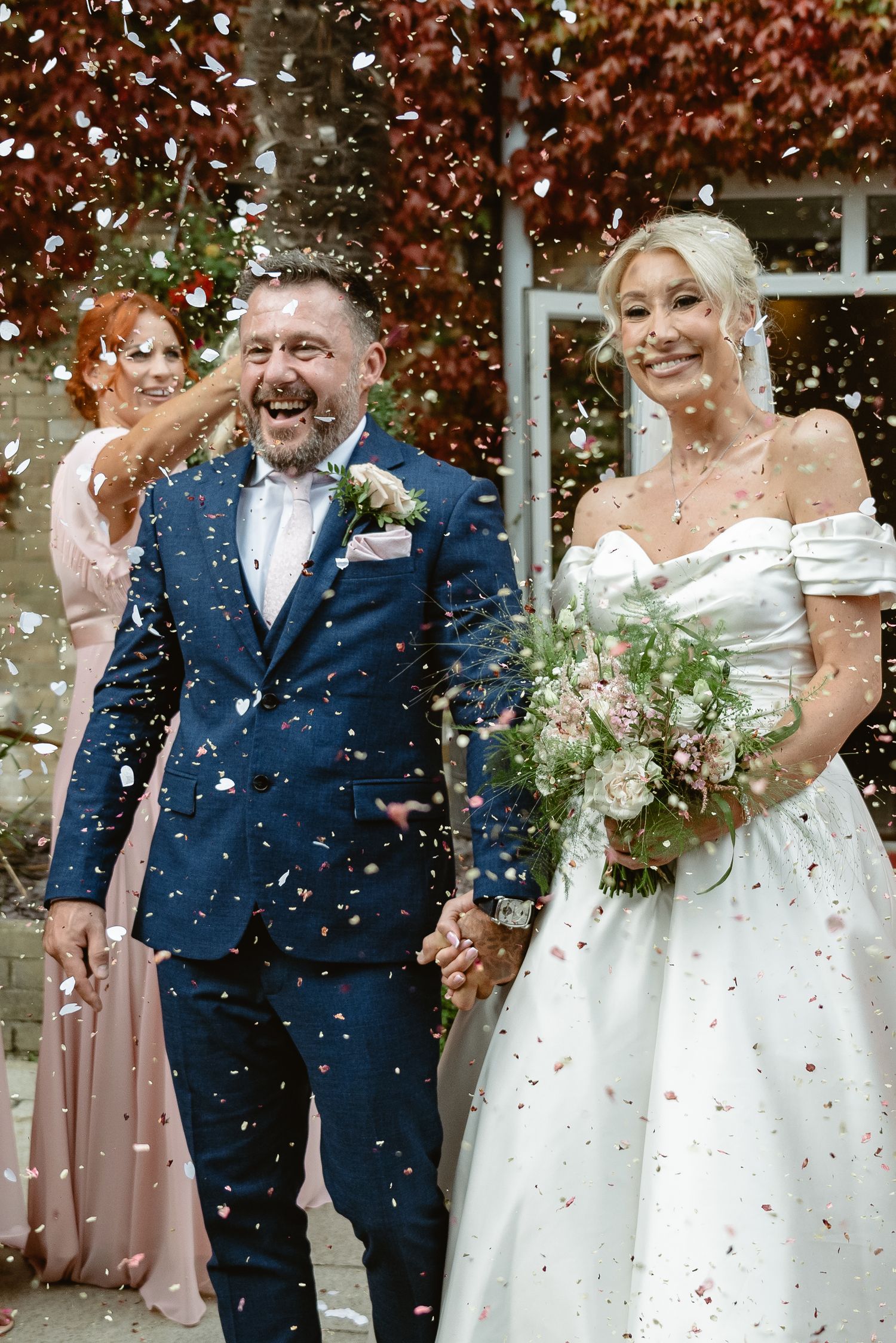 Wedding party celebrates with confetti toss outside brick venue.