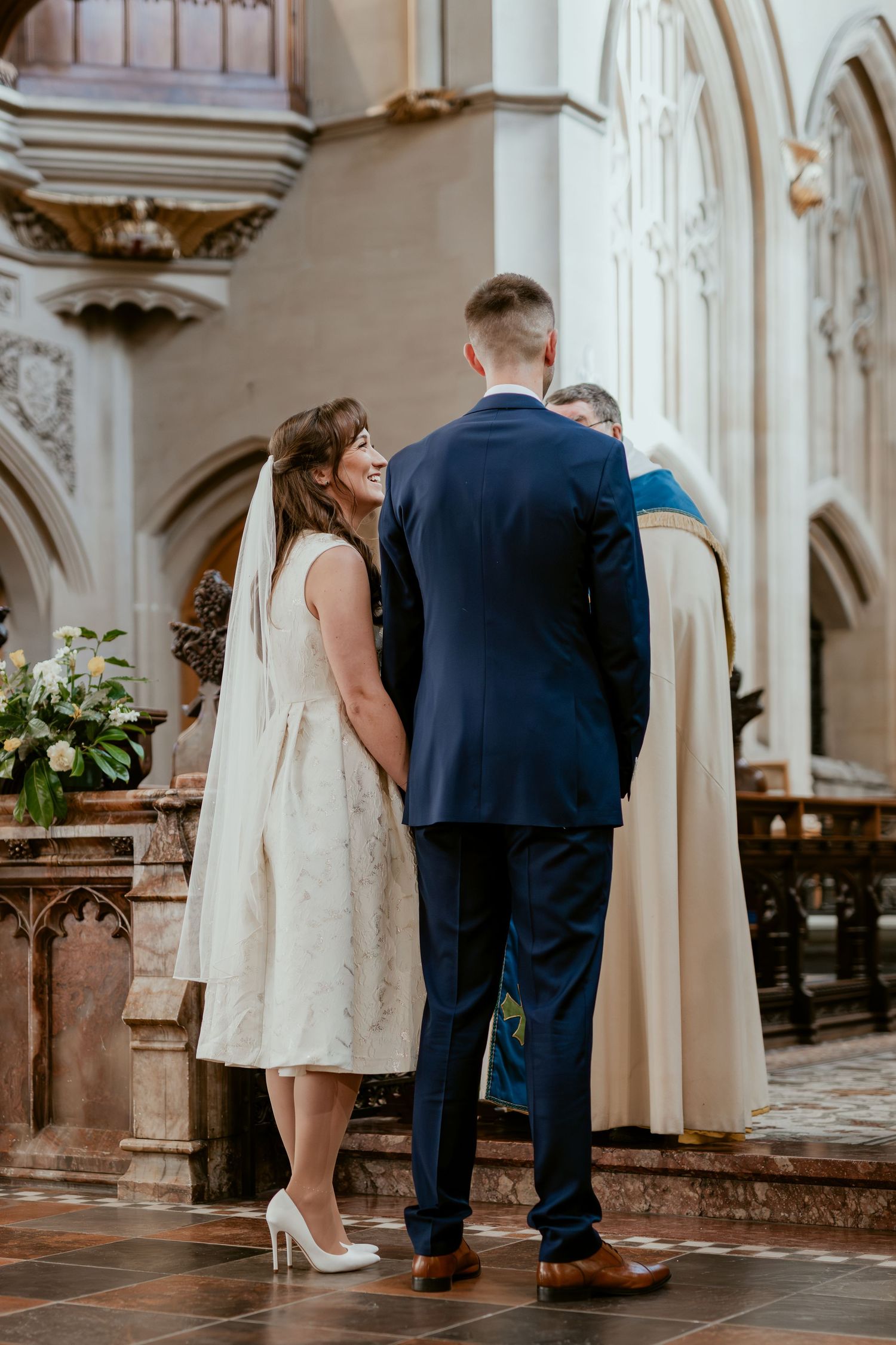 Side view of wedding couple during ceremony in historic church with ornate white pillars.