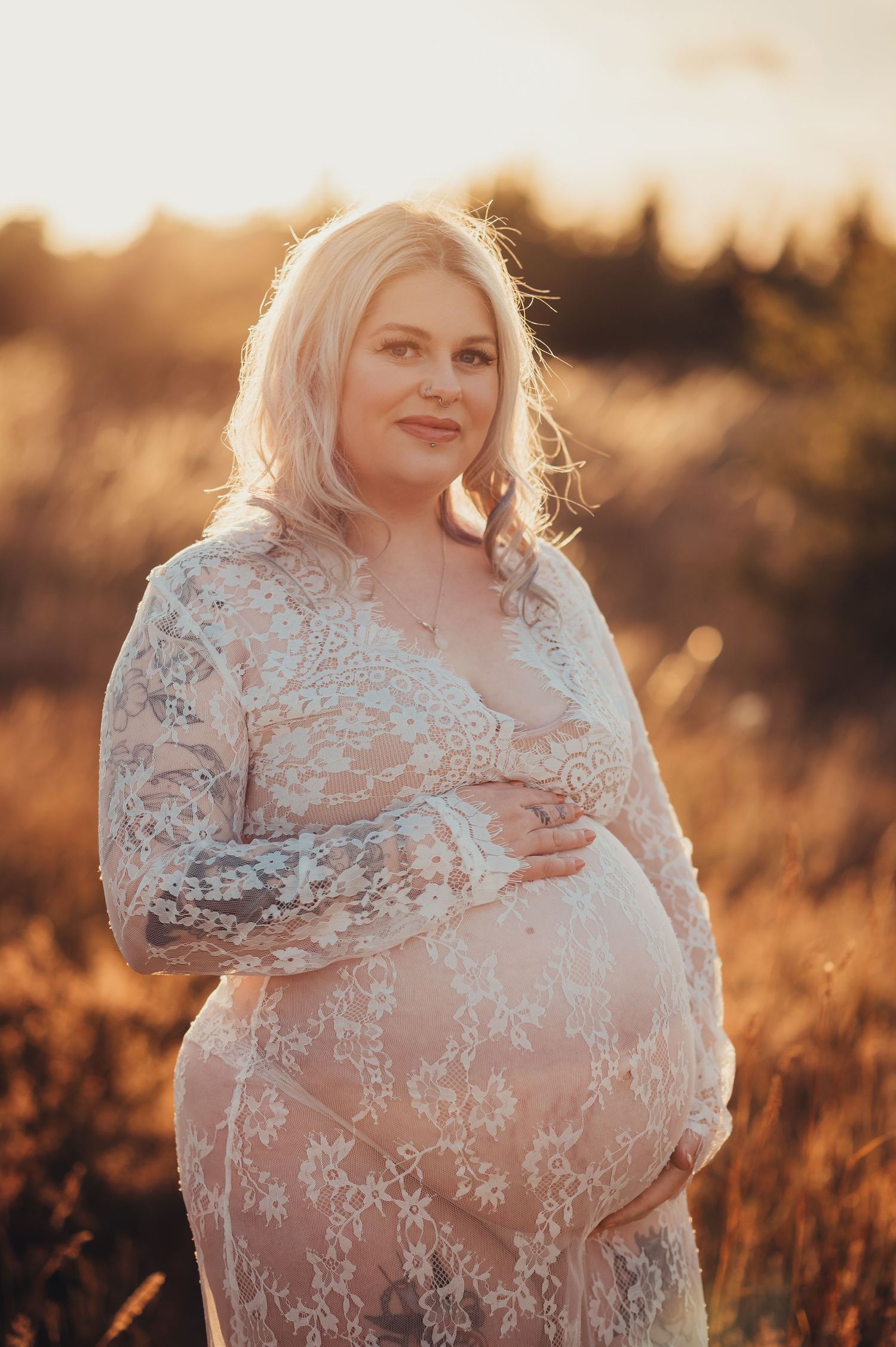 Expectant mother in white lace dress glowing in sunset light.