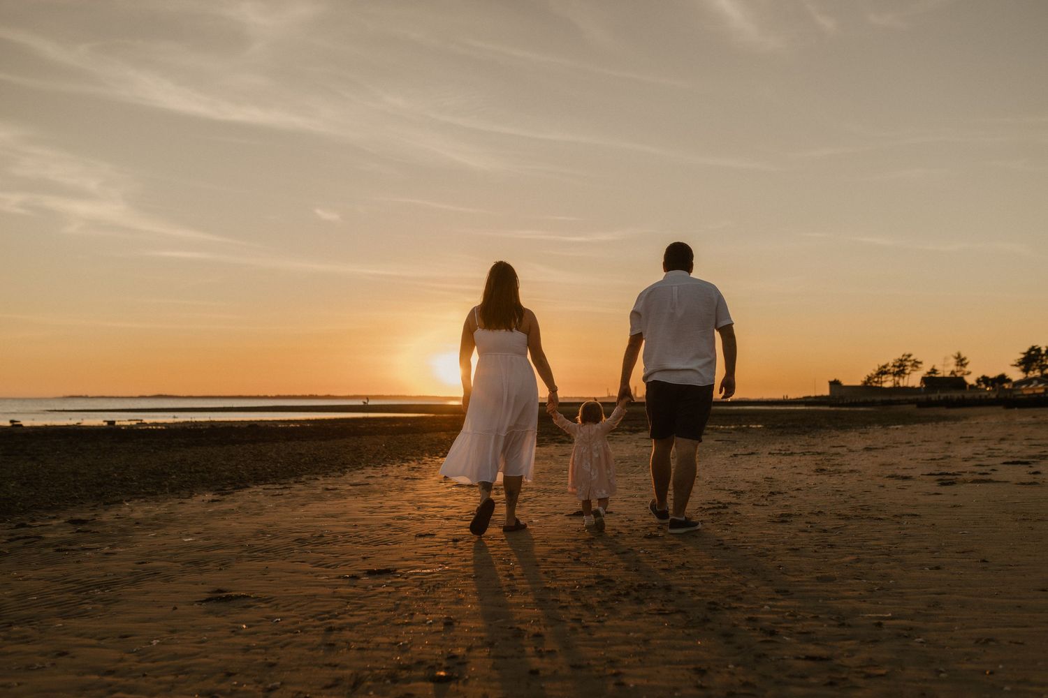 Family silhouettes walking along beach at sunset with child.