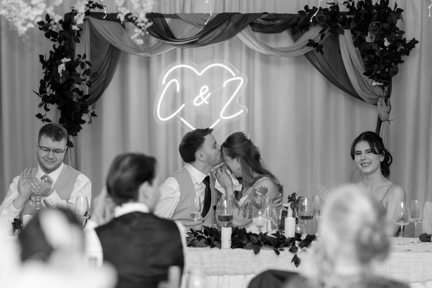 A wedding reception venue decorated with white drapery and floral arrangements while guests celebrate at tables.