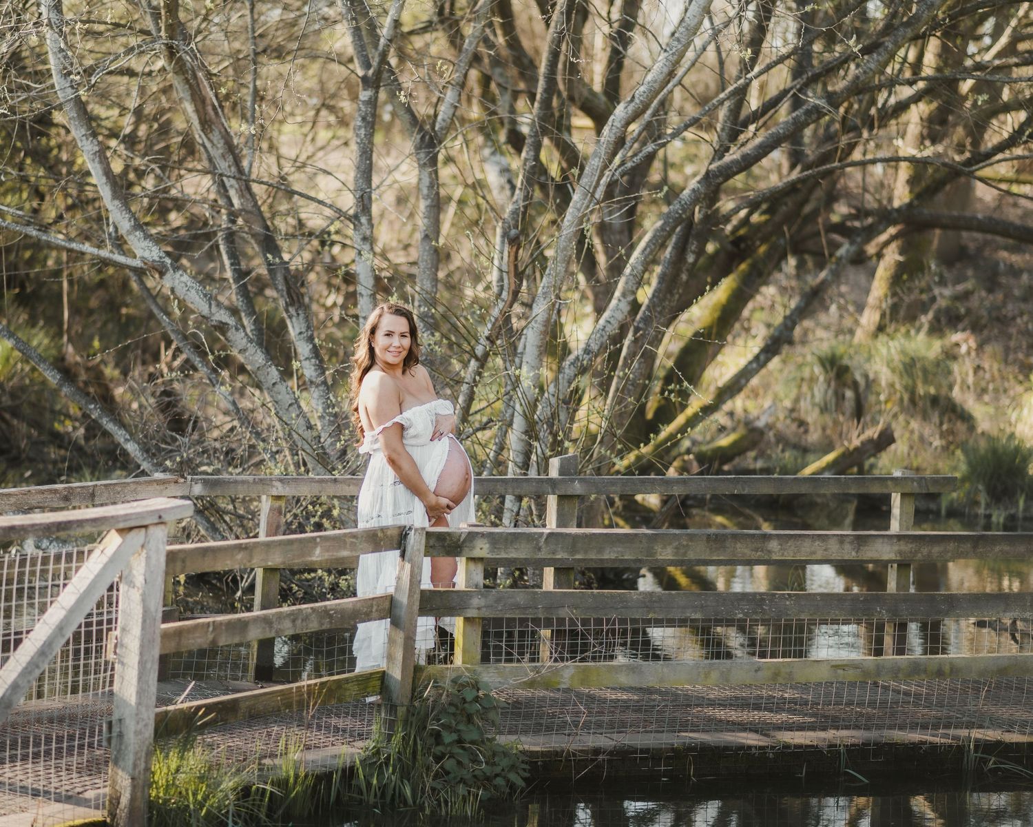 Maternity photoshoot on a wooden bridge surrounded by blooming trees.