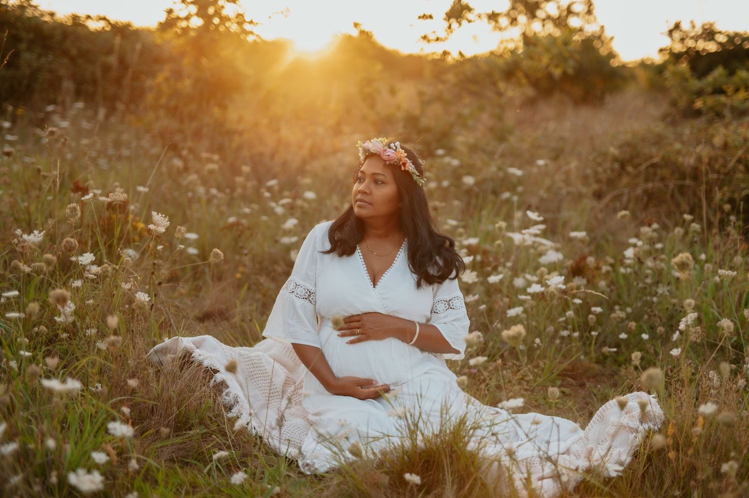 Golden hour maternity session featuring white dress in blooming wildflower field.