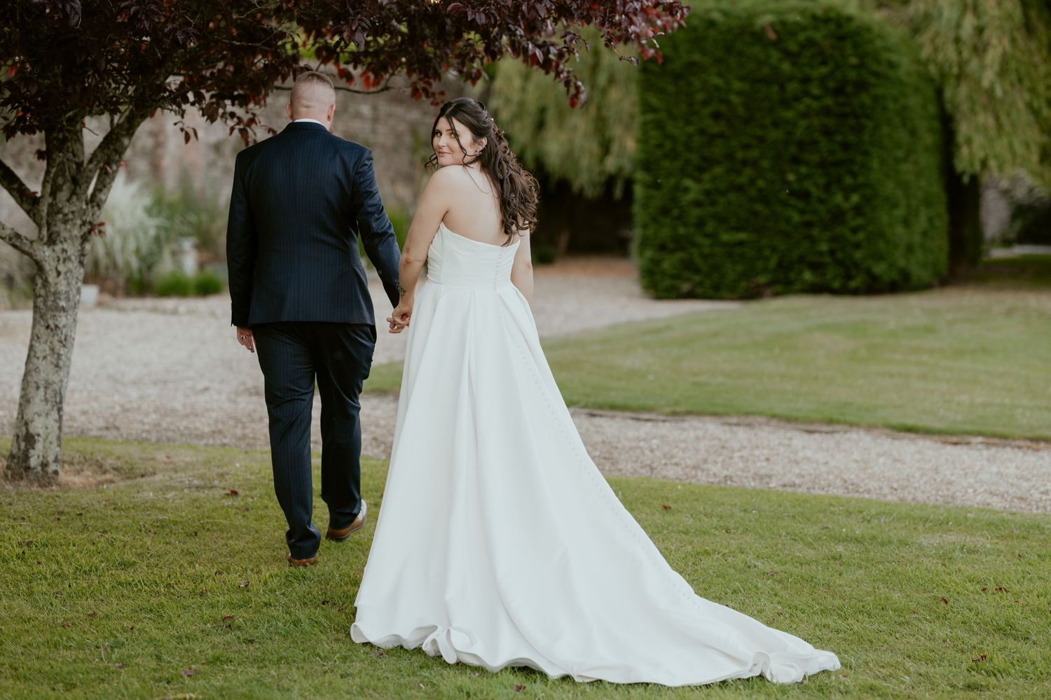 Newlyweds walking together on a garden path surrounded by greenery.