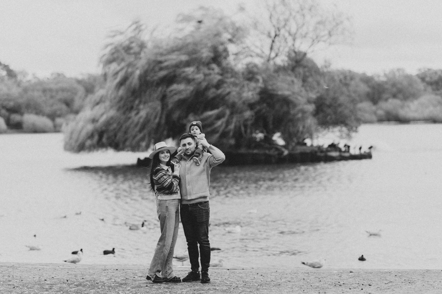 Black and white landscape photo of couple walking along misty waterfront with ducks.