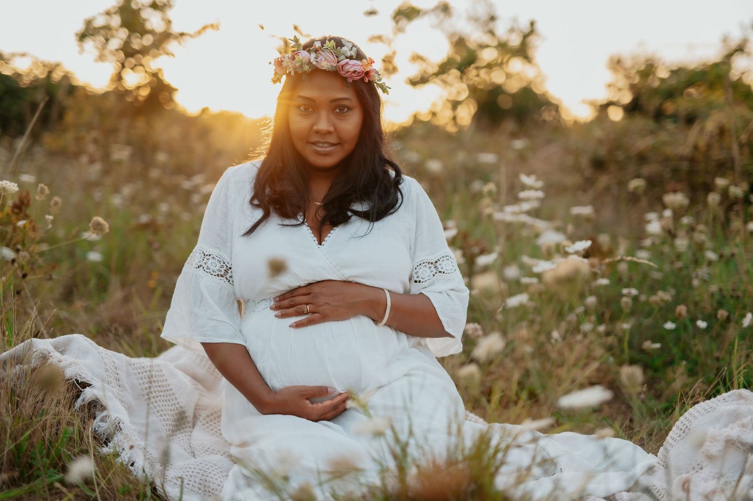 Sunset maternity photography in white dress surrounded by wildflowers.