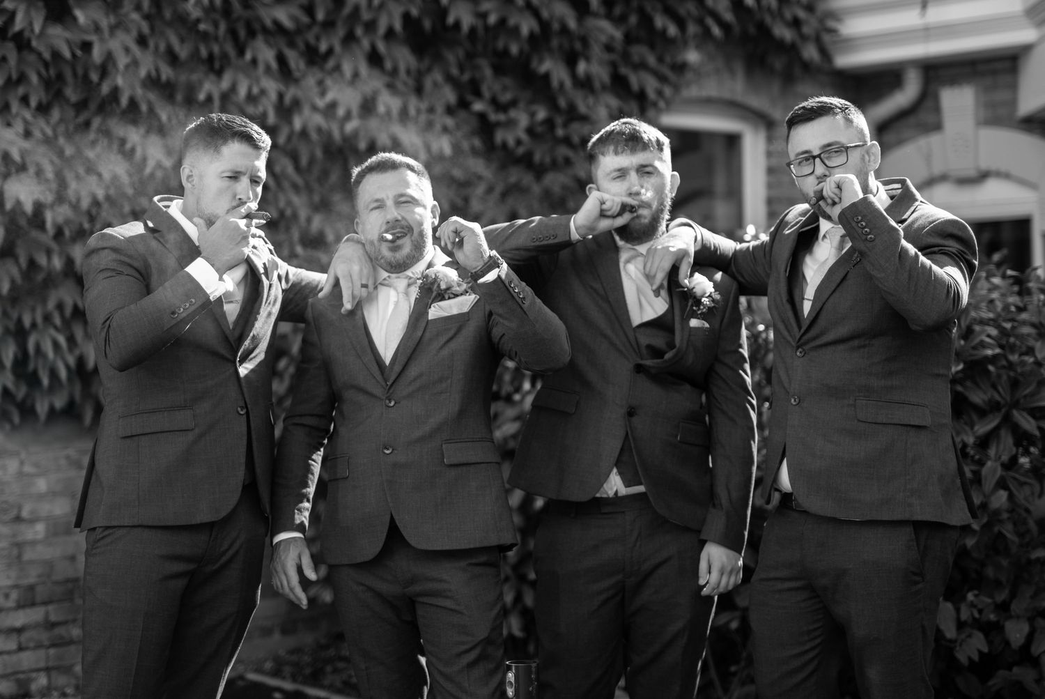Groomsmen in dark suits share laughs during outdoor wedding photo session.