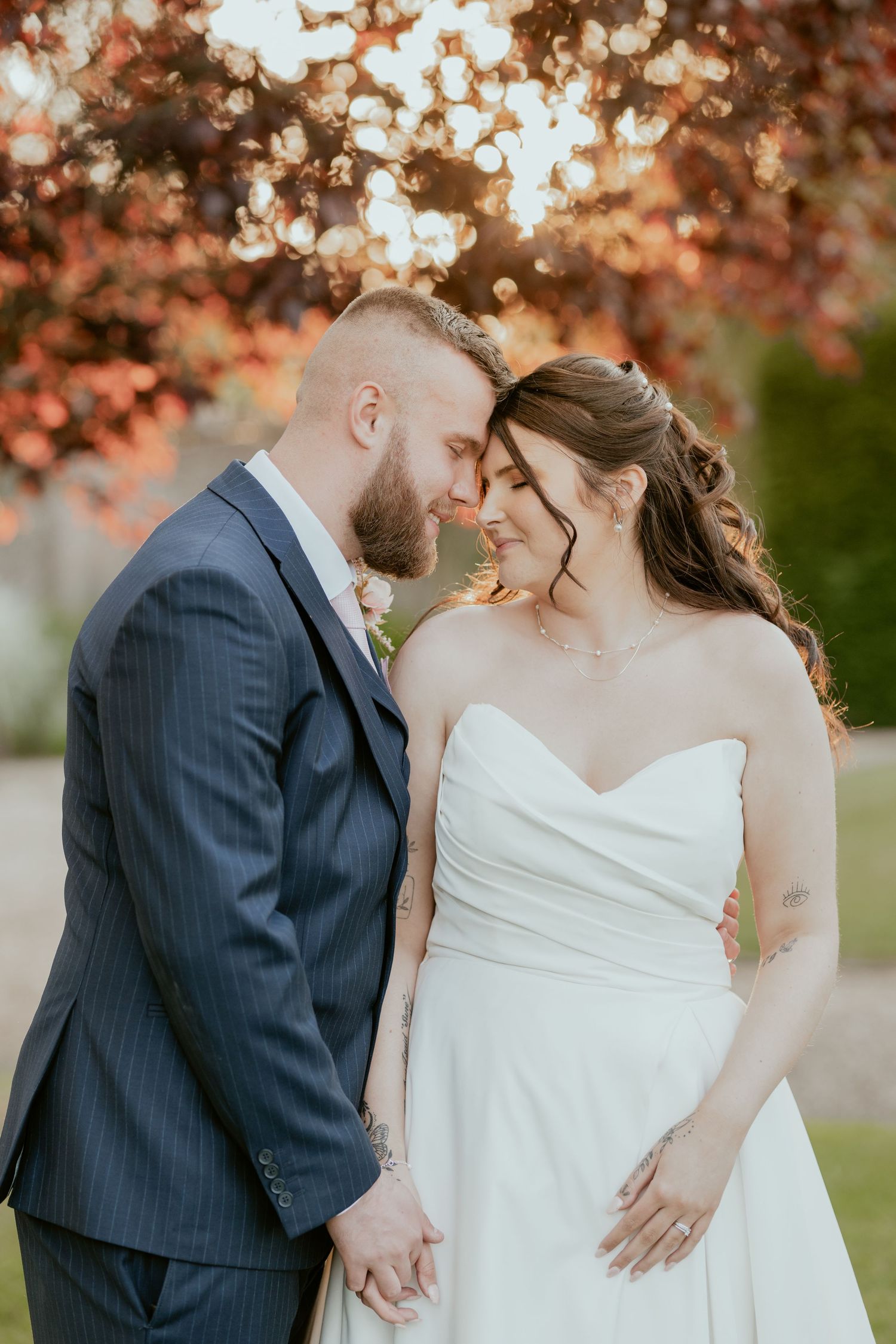 Romantic wedding couple embracing under autumn trees with soft golden light filtering through.