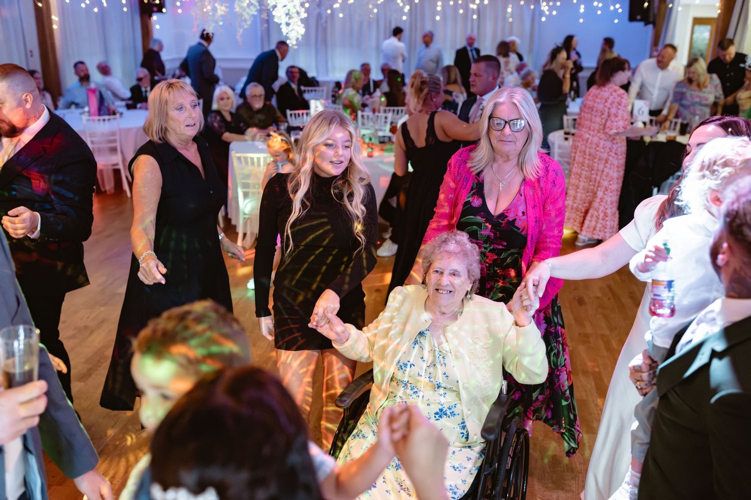 Lively wedding reception dance floor with guests dancing under twinkling lights and festive decorations.