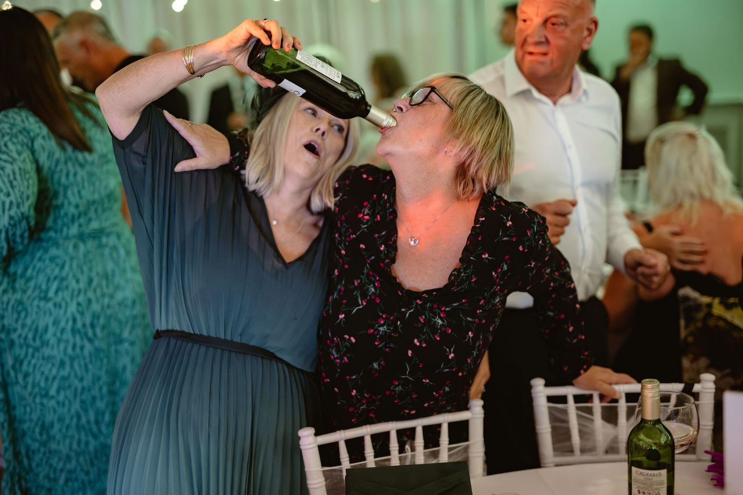 Wedding guests enjoying lively dancing at reception under ambient green lighting.