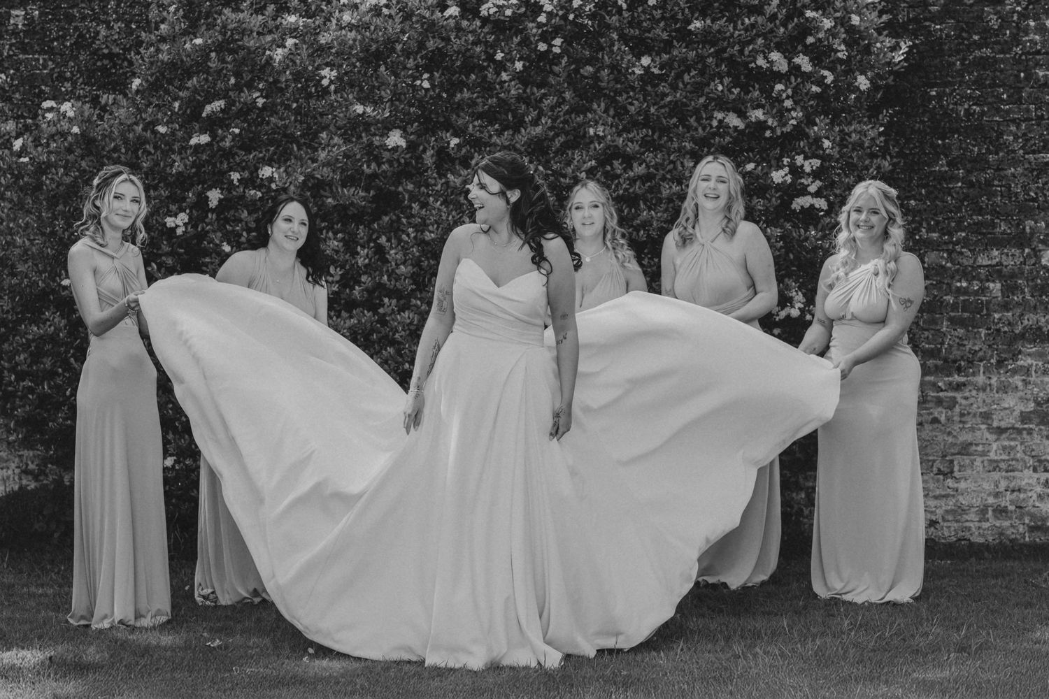 Black and white photo of bridesmaids arranging wedding dress train outdoors.