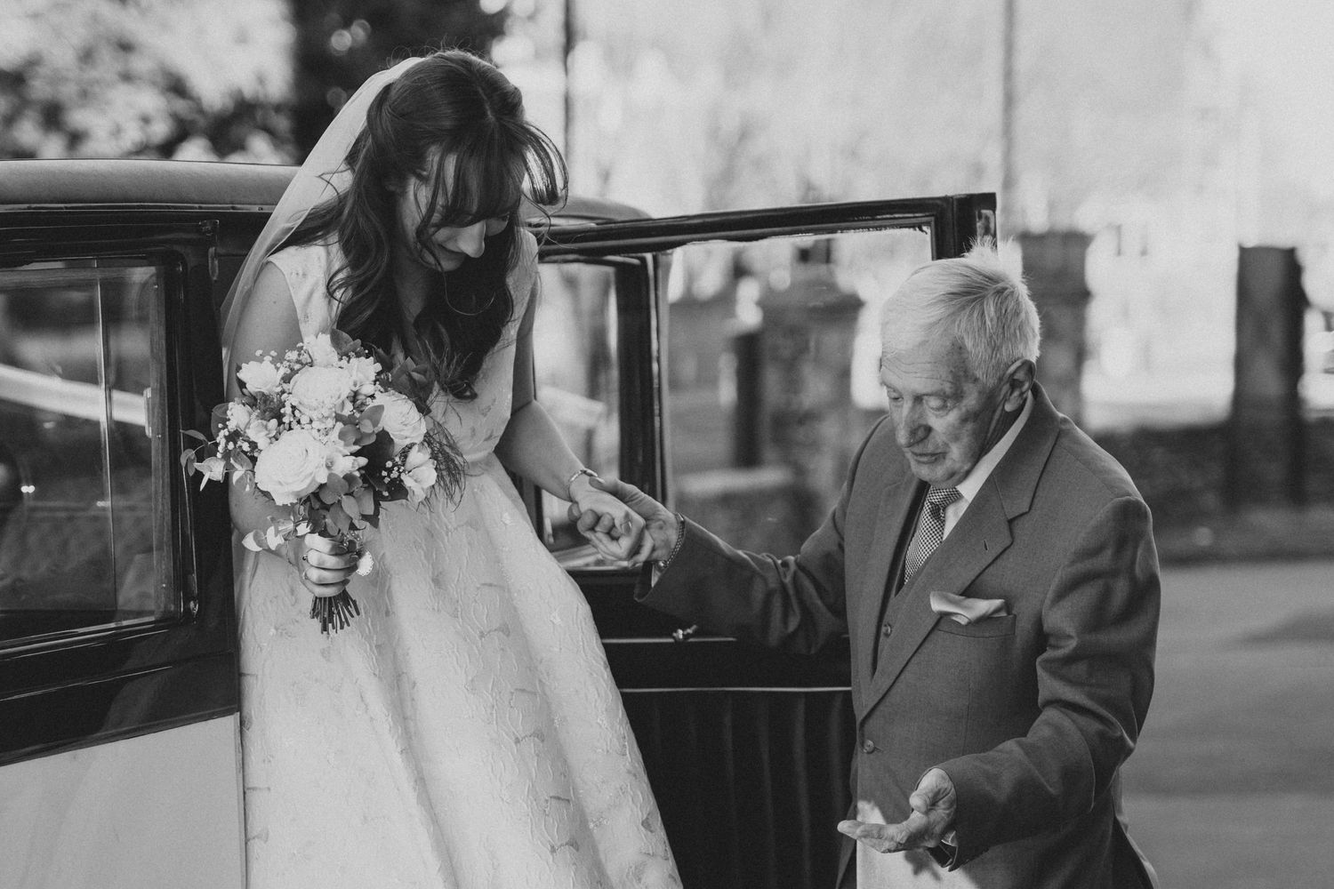 A vintage wedding scene with a classic car and formal attire.