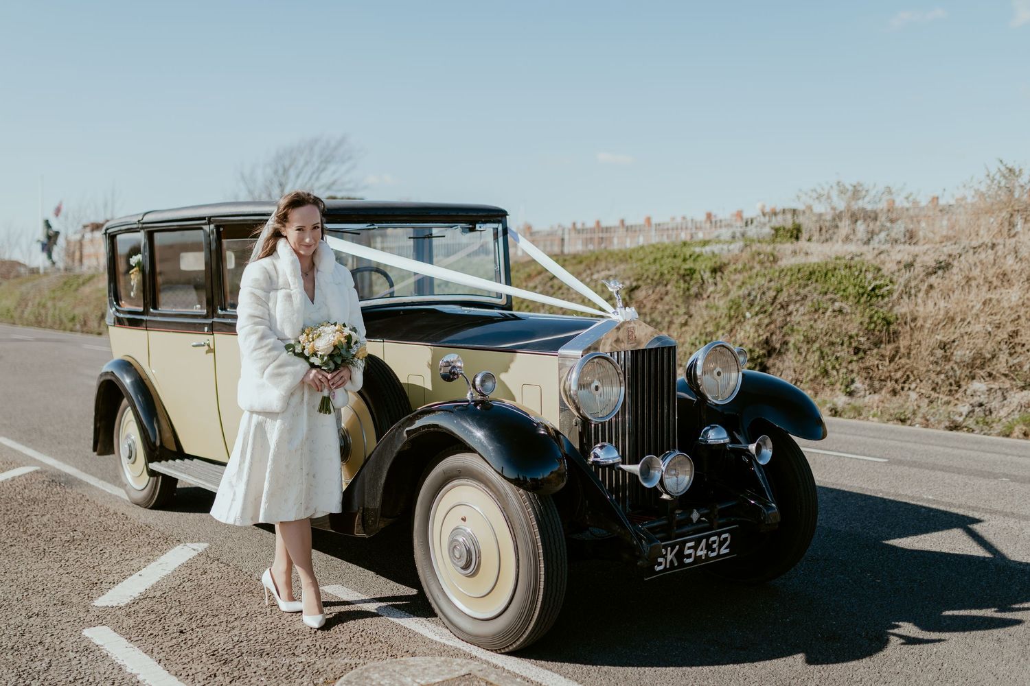 A classic cream and black vintage car parked on a gravel lot.