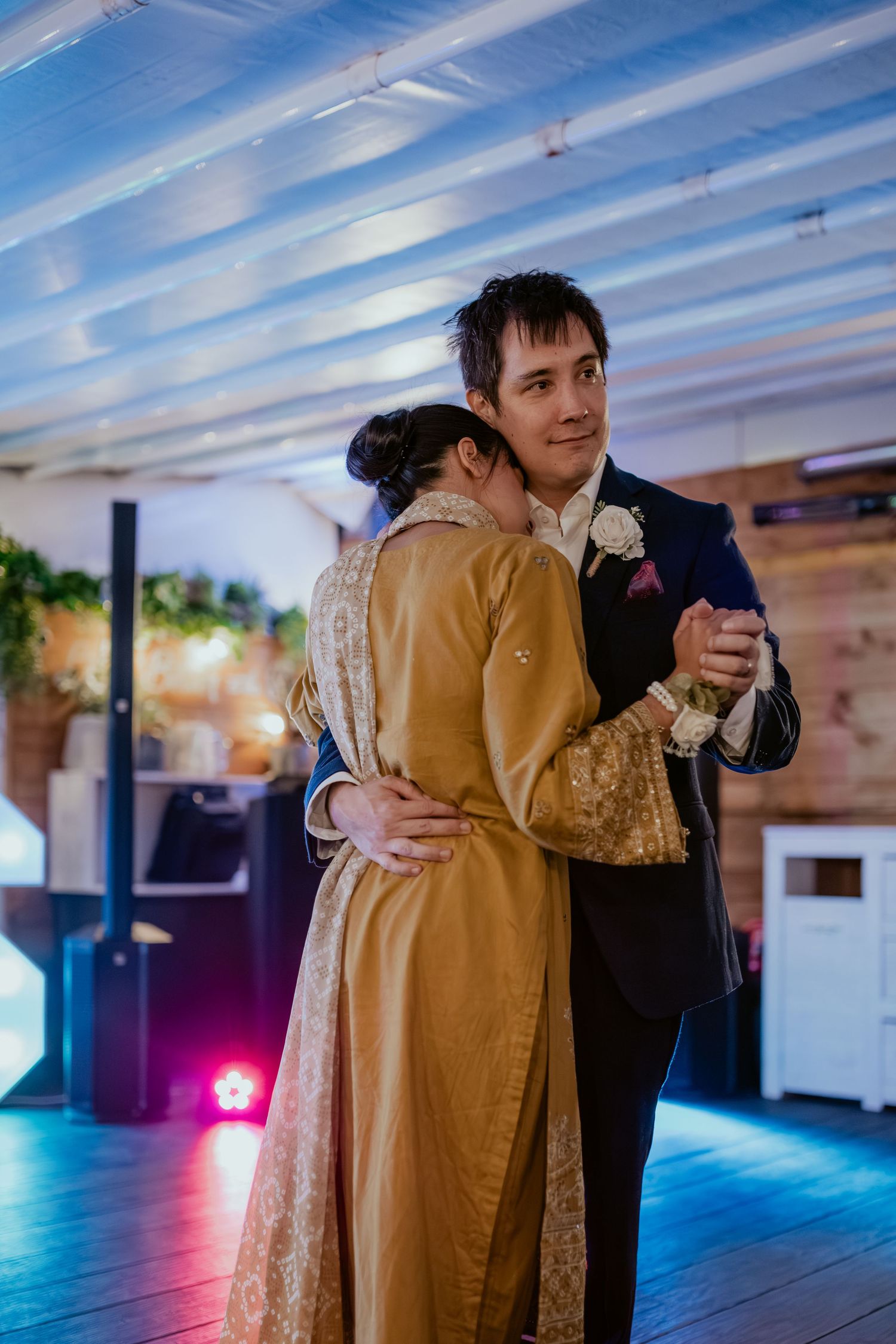 Couple dancing under blue lighting at indoor wedding reception venue.