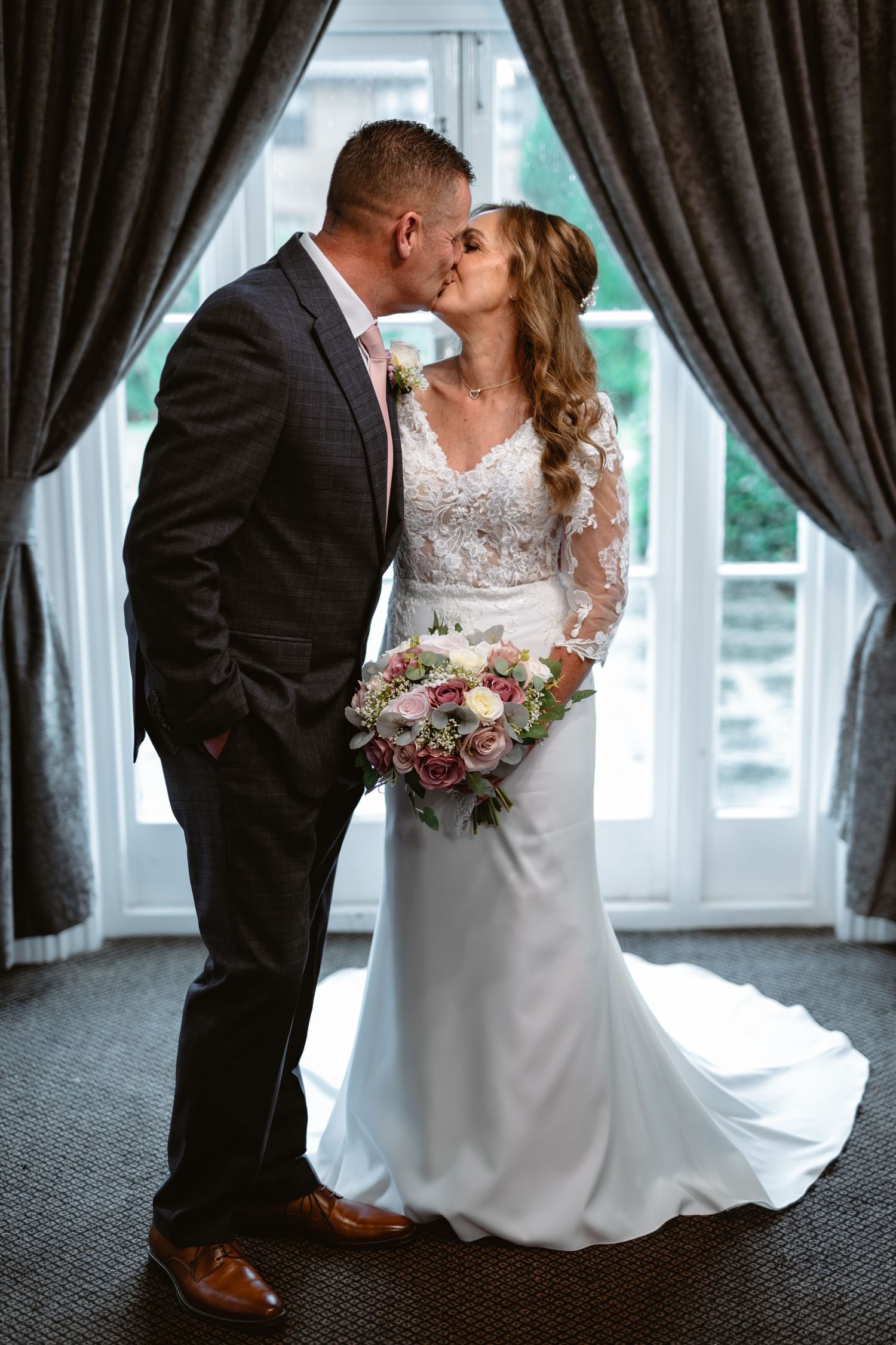 Romantic wedding couple embracing in front of elegant dark curtains.