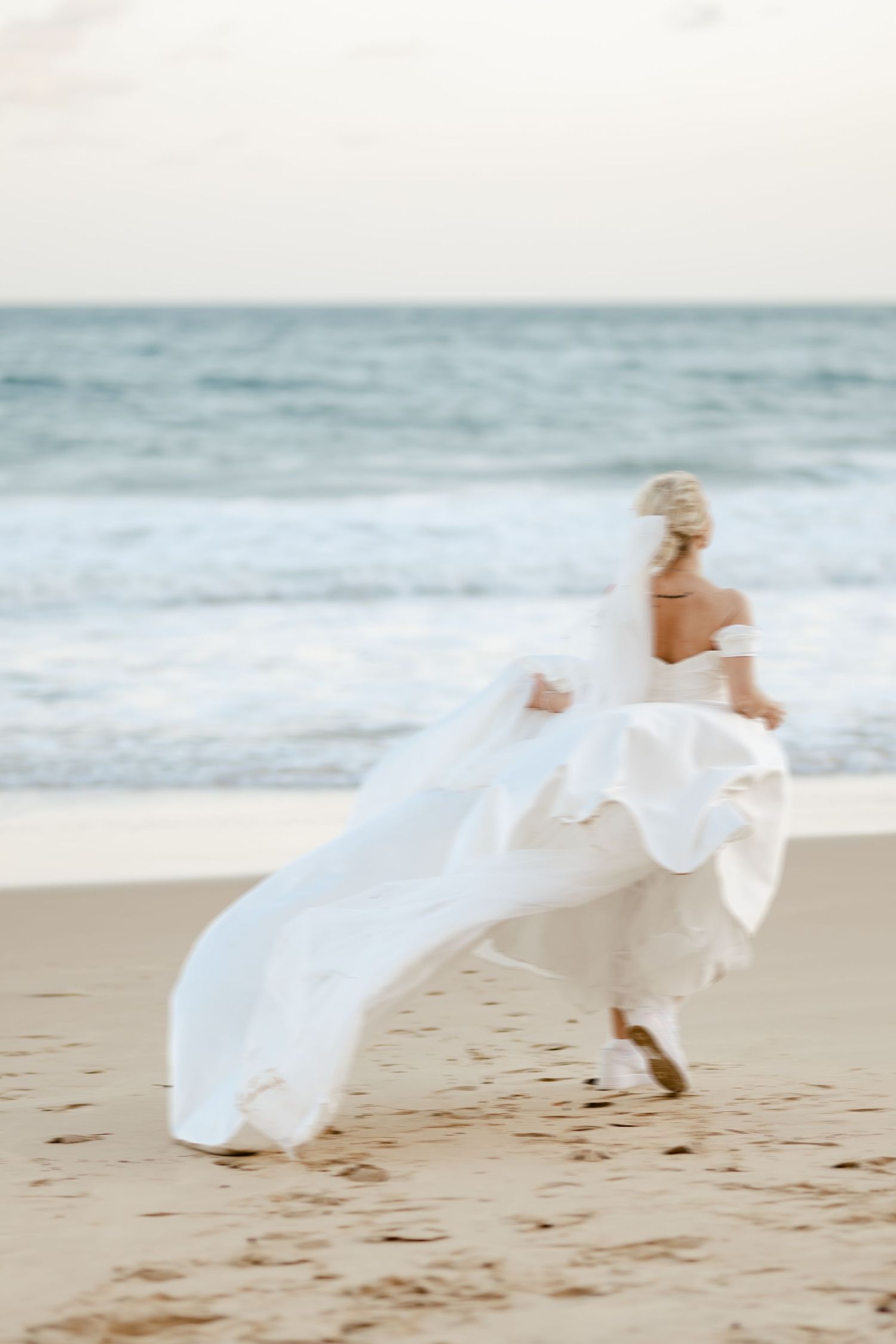 Ethereal bridal photos on beach with flowing white dress catching ocean breeze.