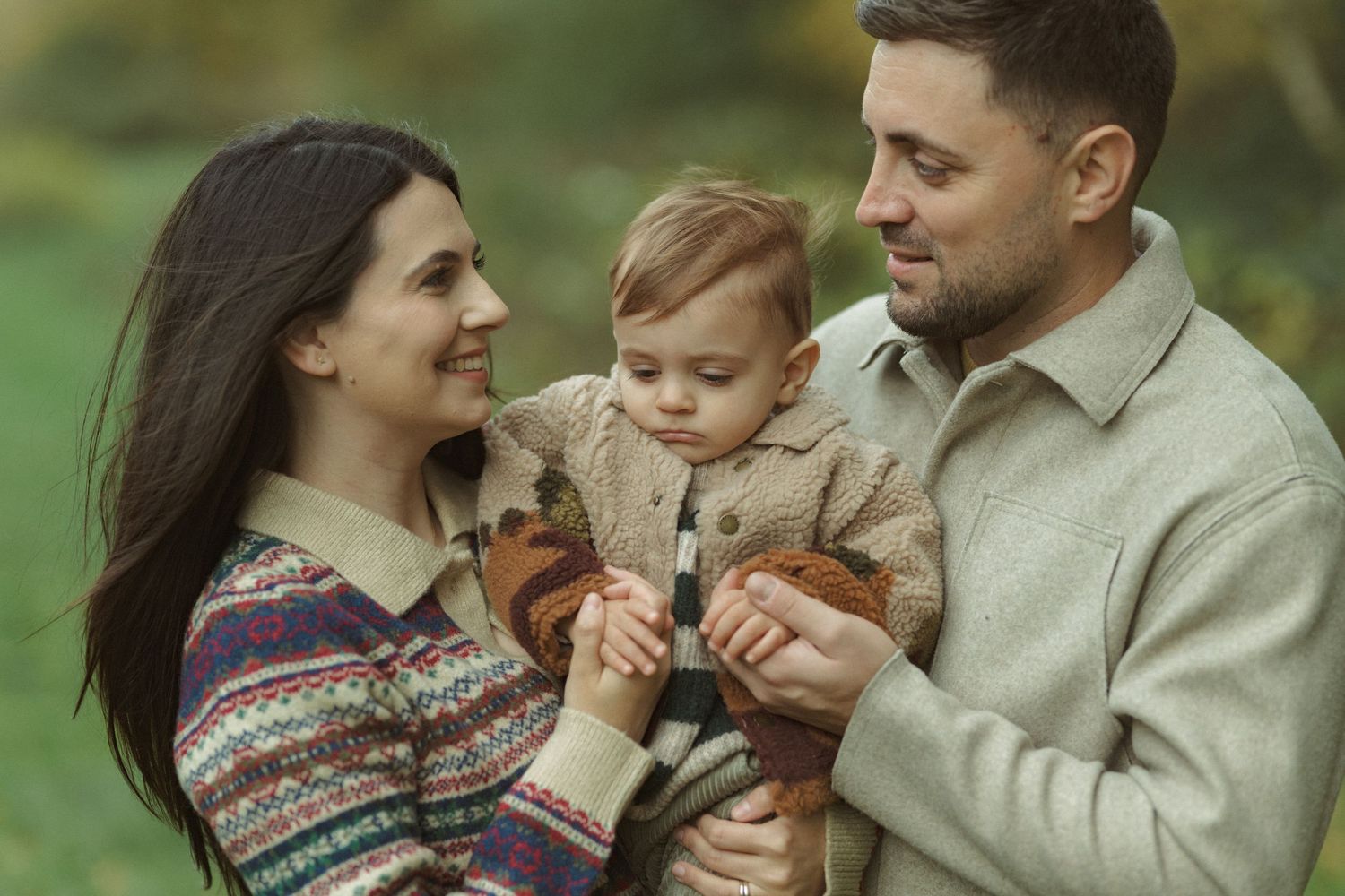 A tender family moment captured outdoors during autumn with fall colors in the background.