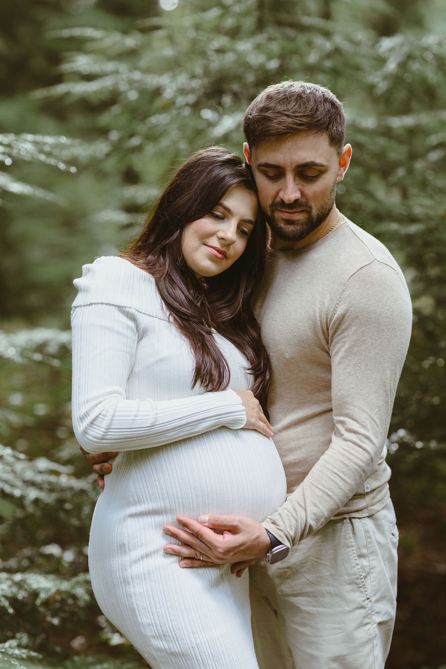 A couple shares loving moments during their maternity photoshoot in a sunlit forest.