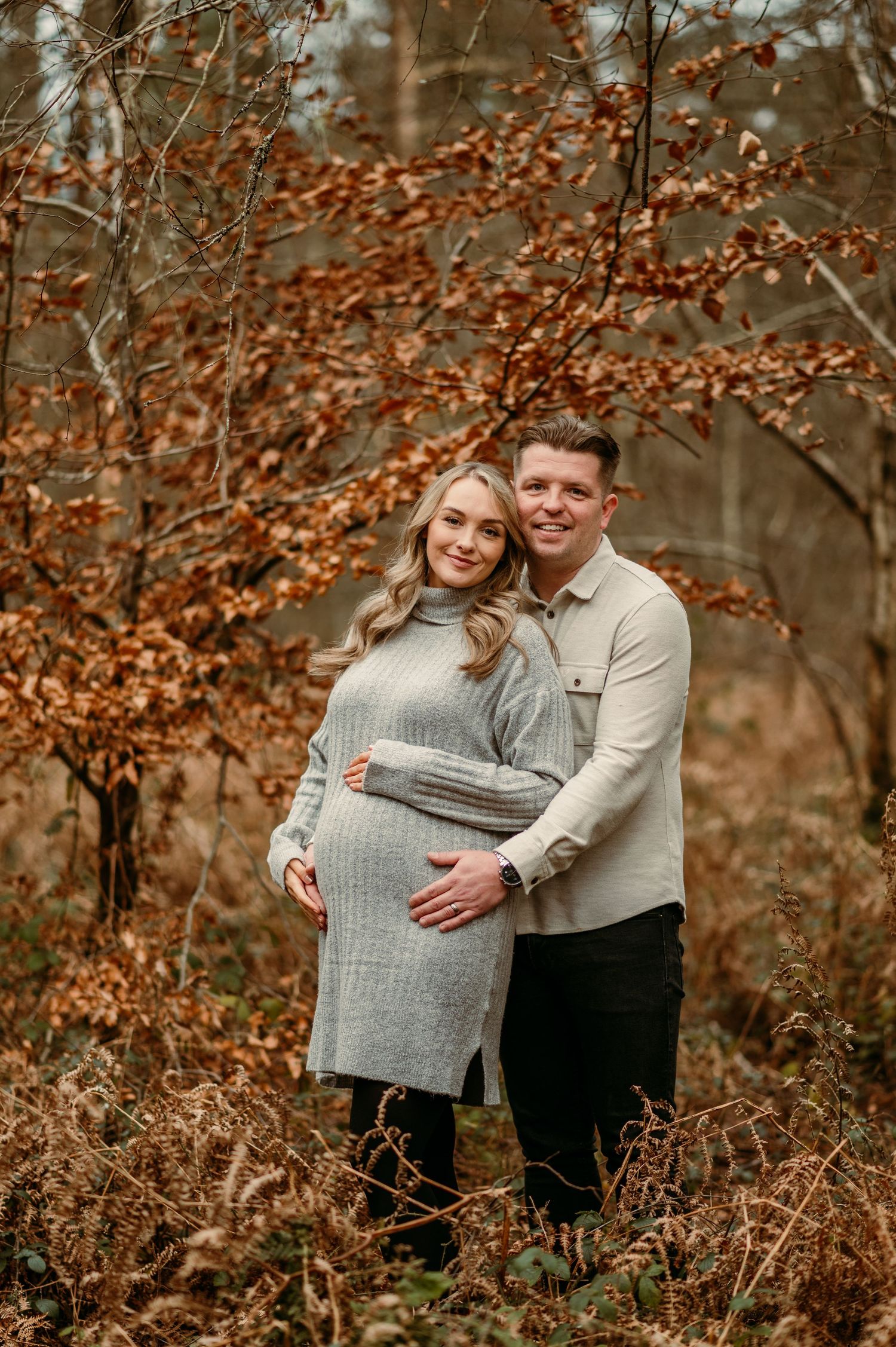 A couple shares tender moments during their maternity photoshoot in a fall forest setting.