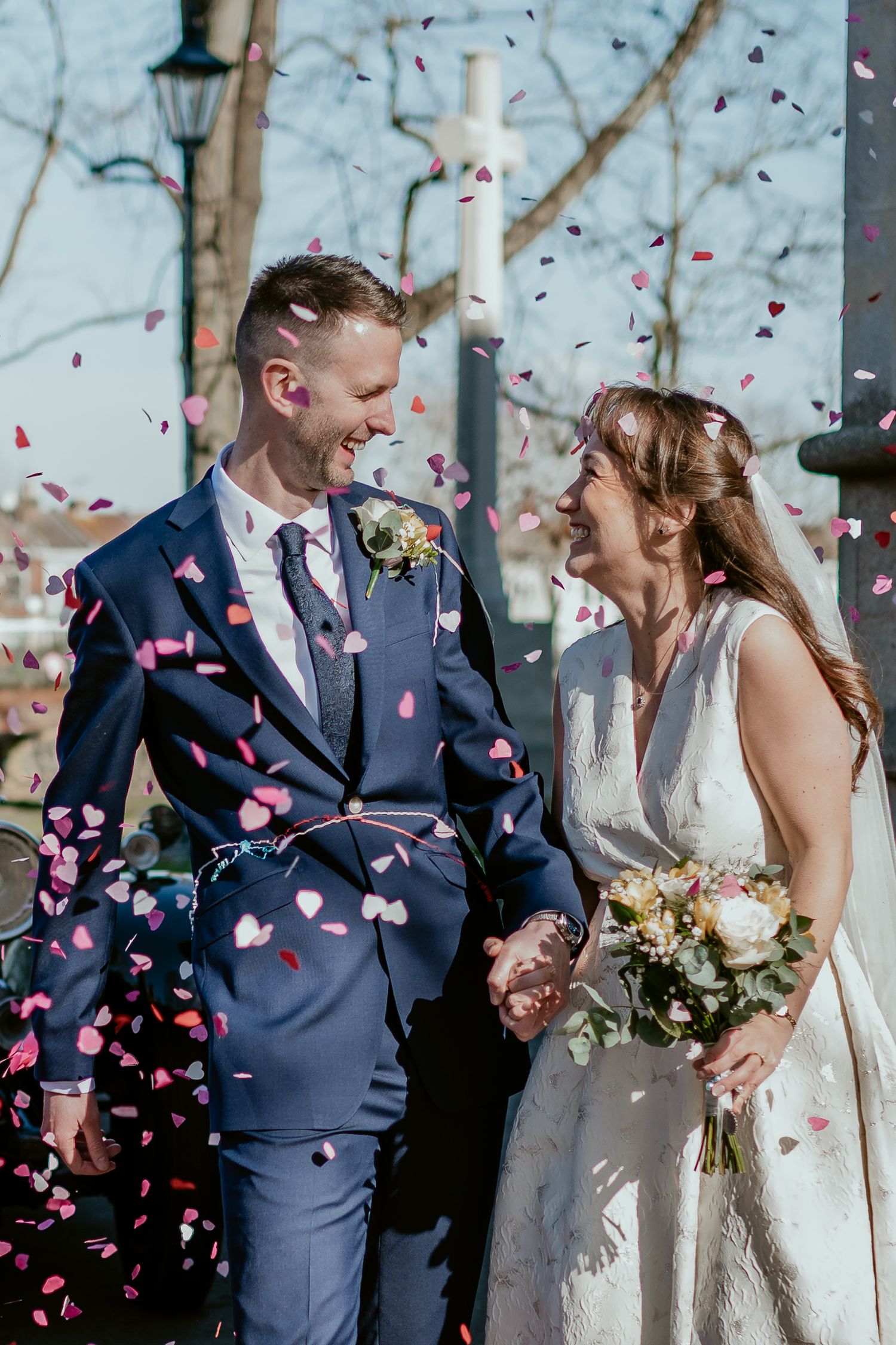 Wedding couple celebrates under falling pink confetti petals outdoors.