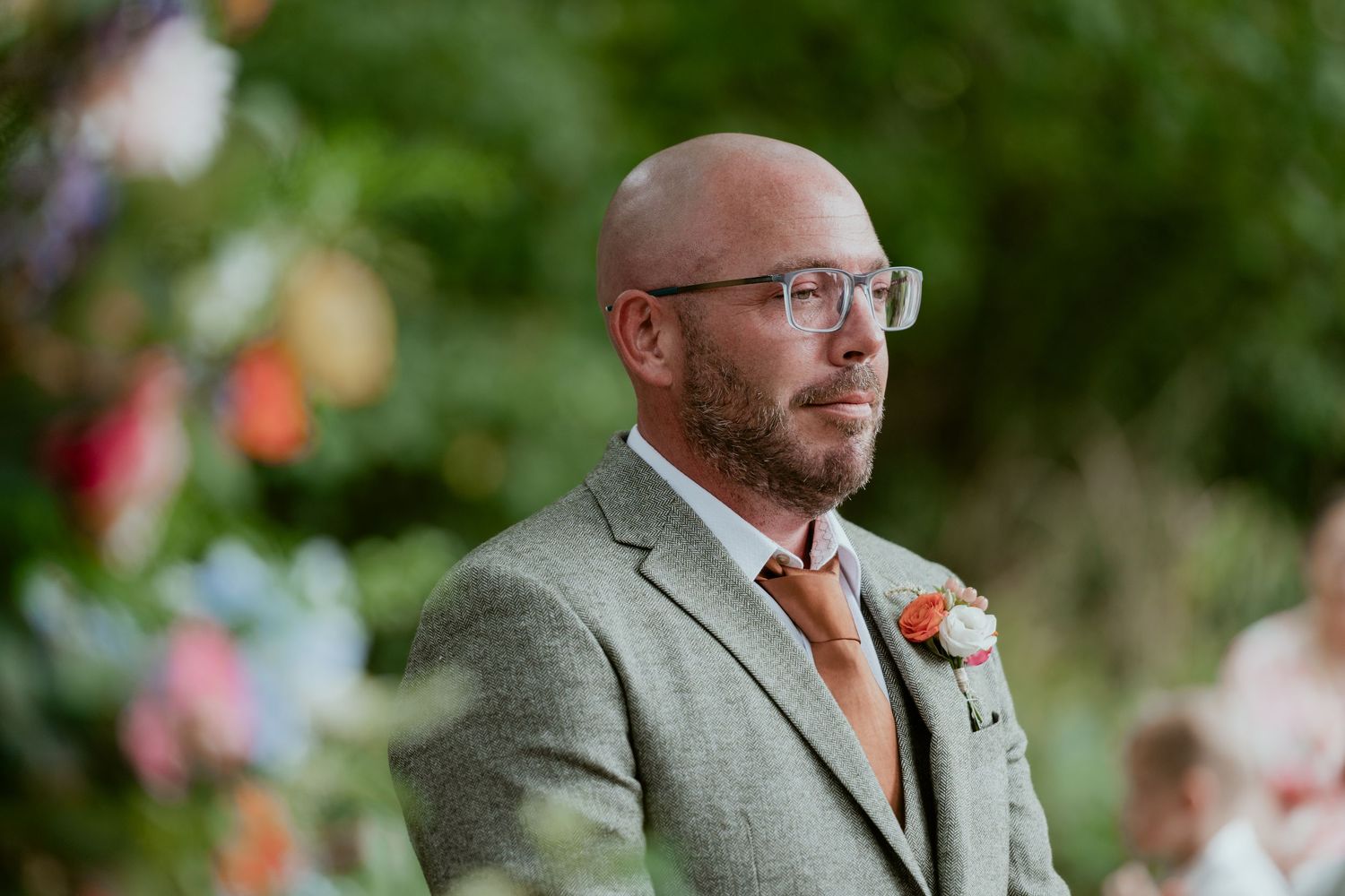 Wedding guest in gray suit and glasses with coral boutonniere.