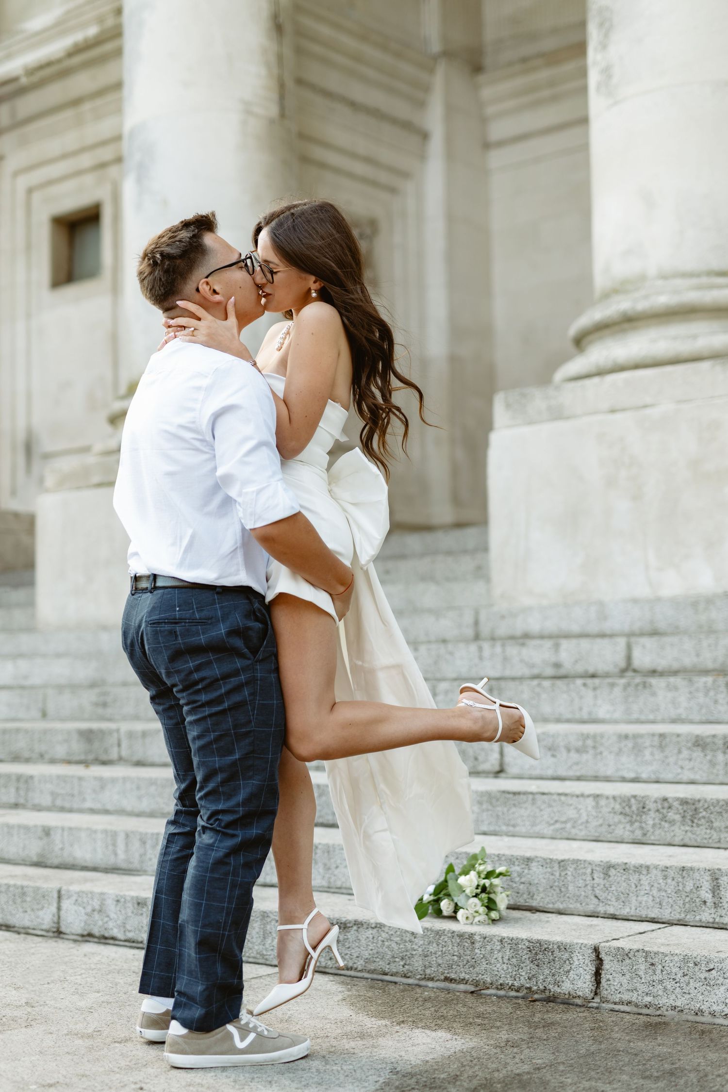 Wedding couple sharing an intimate moment on grand marble steps with a white bouquet.