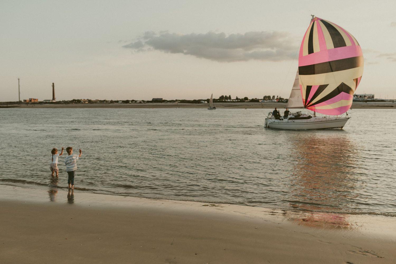 Pink sailboat on water at sunset with beach in foreground.