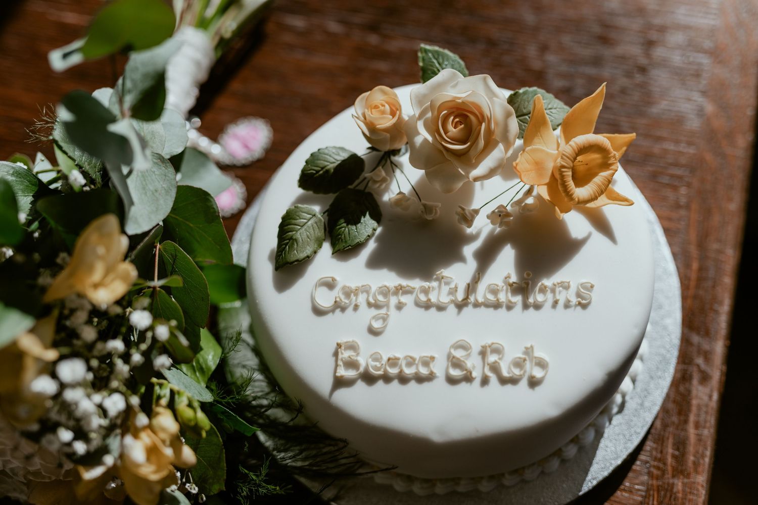 Wedding cake decorated with delicate gold roses and white frosting on a wooden surface.