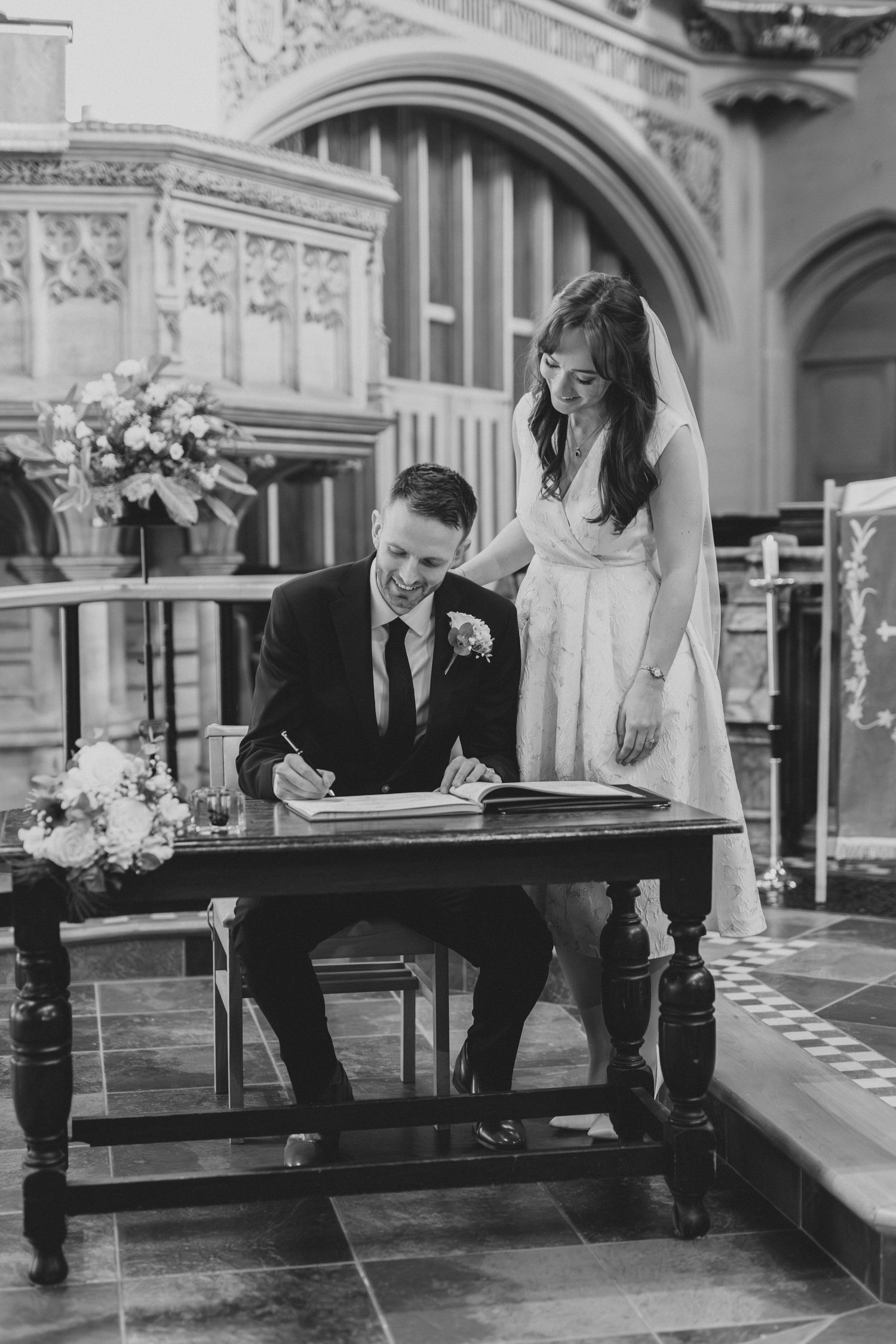 Couple signing marriage register in black and white at traditional church ceremony.