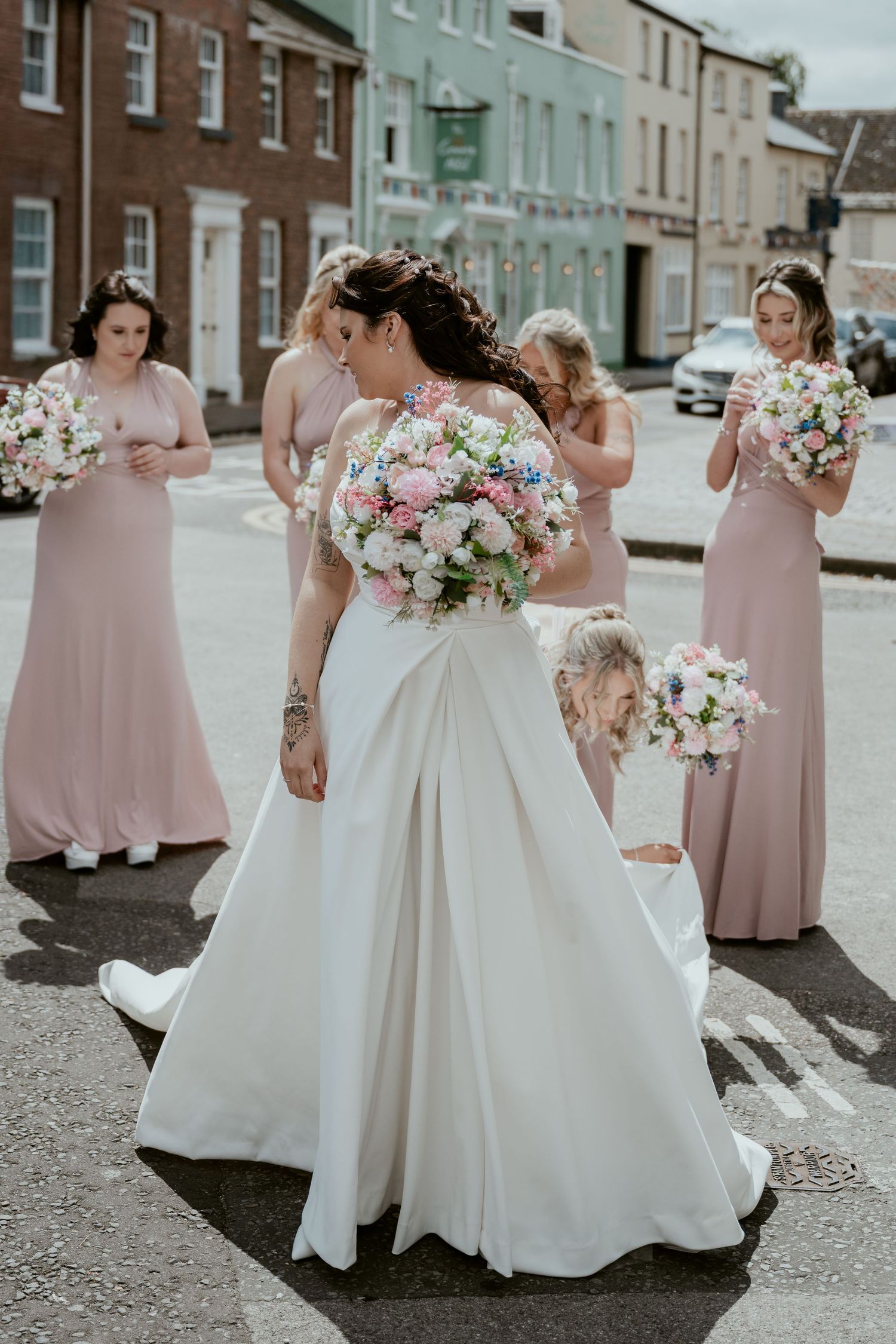 Bridesmaids in blush pink dresses pose with wedding bouquets on a city street.
