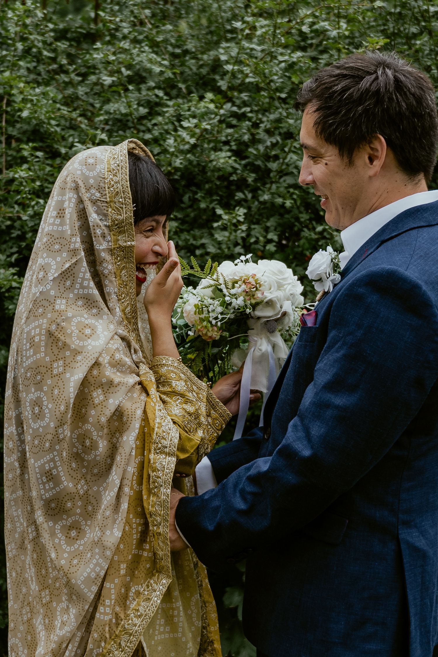 Couple sharing an intimate moment in a garden setting with bride wearing traditional gold veil.