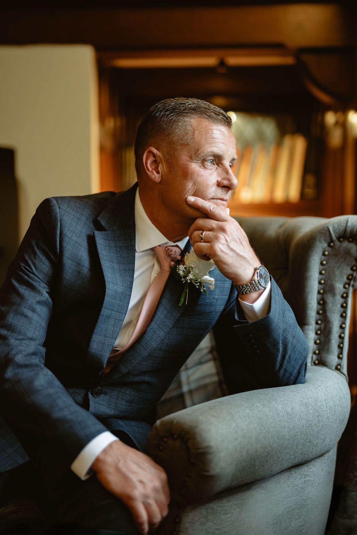 Groom in navy suit pensively waiting in library setting.