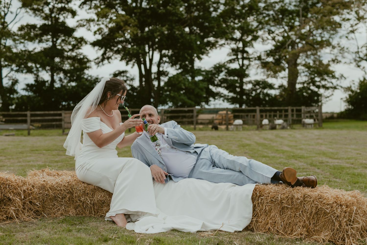 Couple posing for romantic photos on hay bales in a rustic outdoor setting.