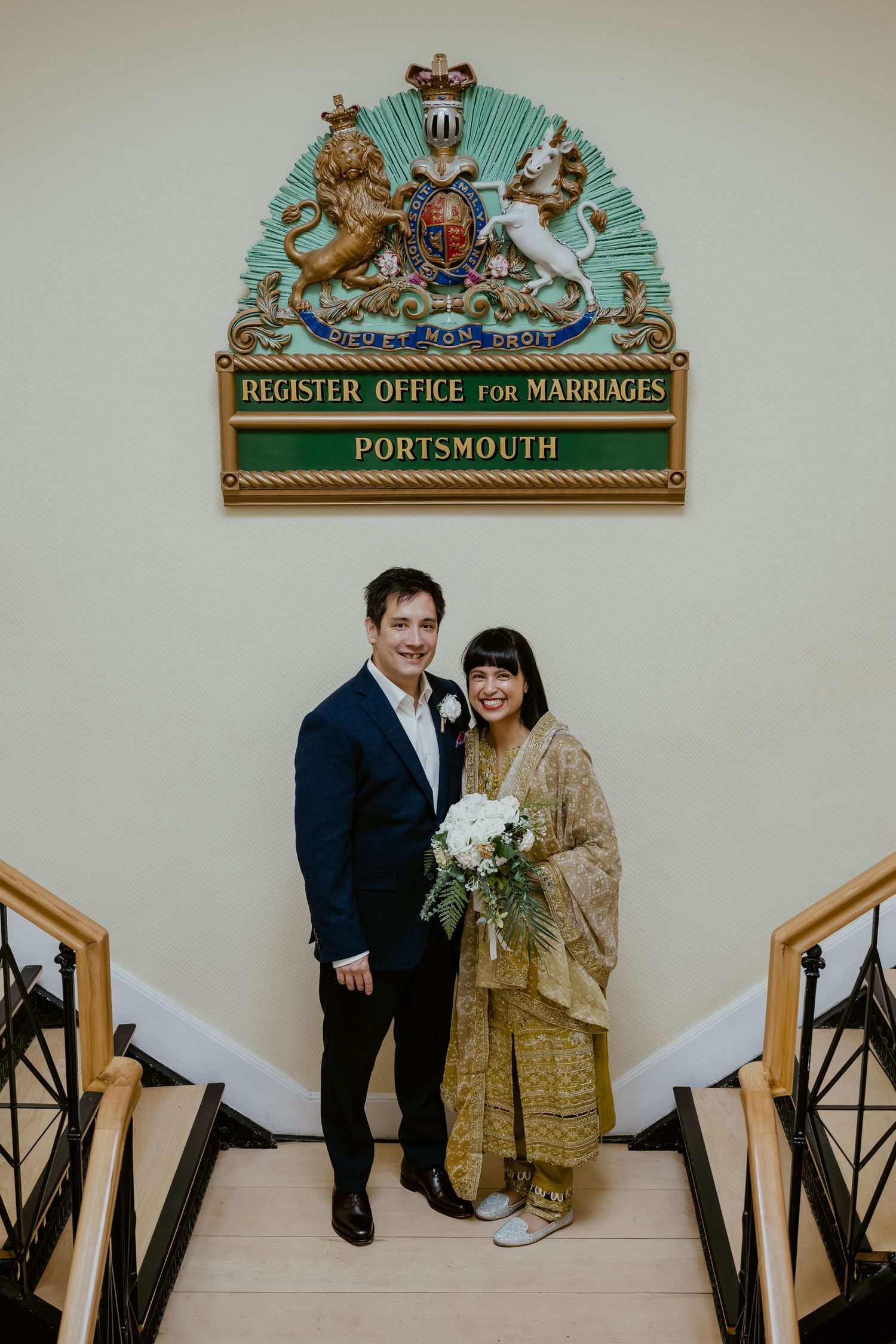 A couple poses beneath the Portsmouth Register Office for Marriages sign featuring a decorative coat of arms.