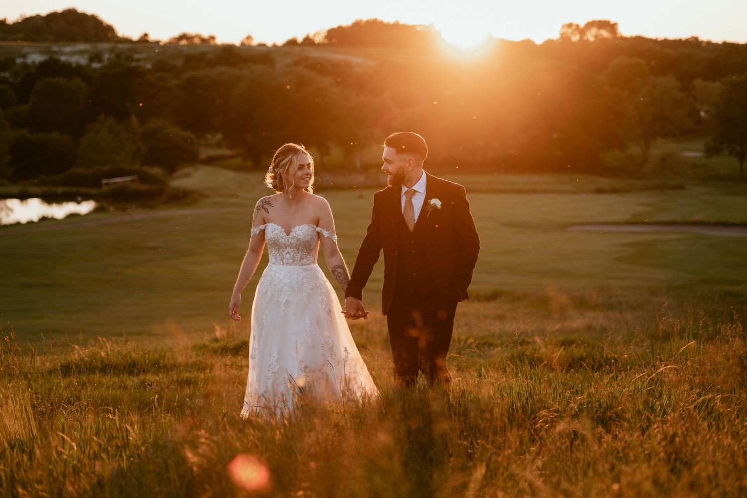Romantic sunset silhouette of couple walking through golden field with sun flare.