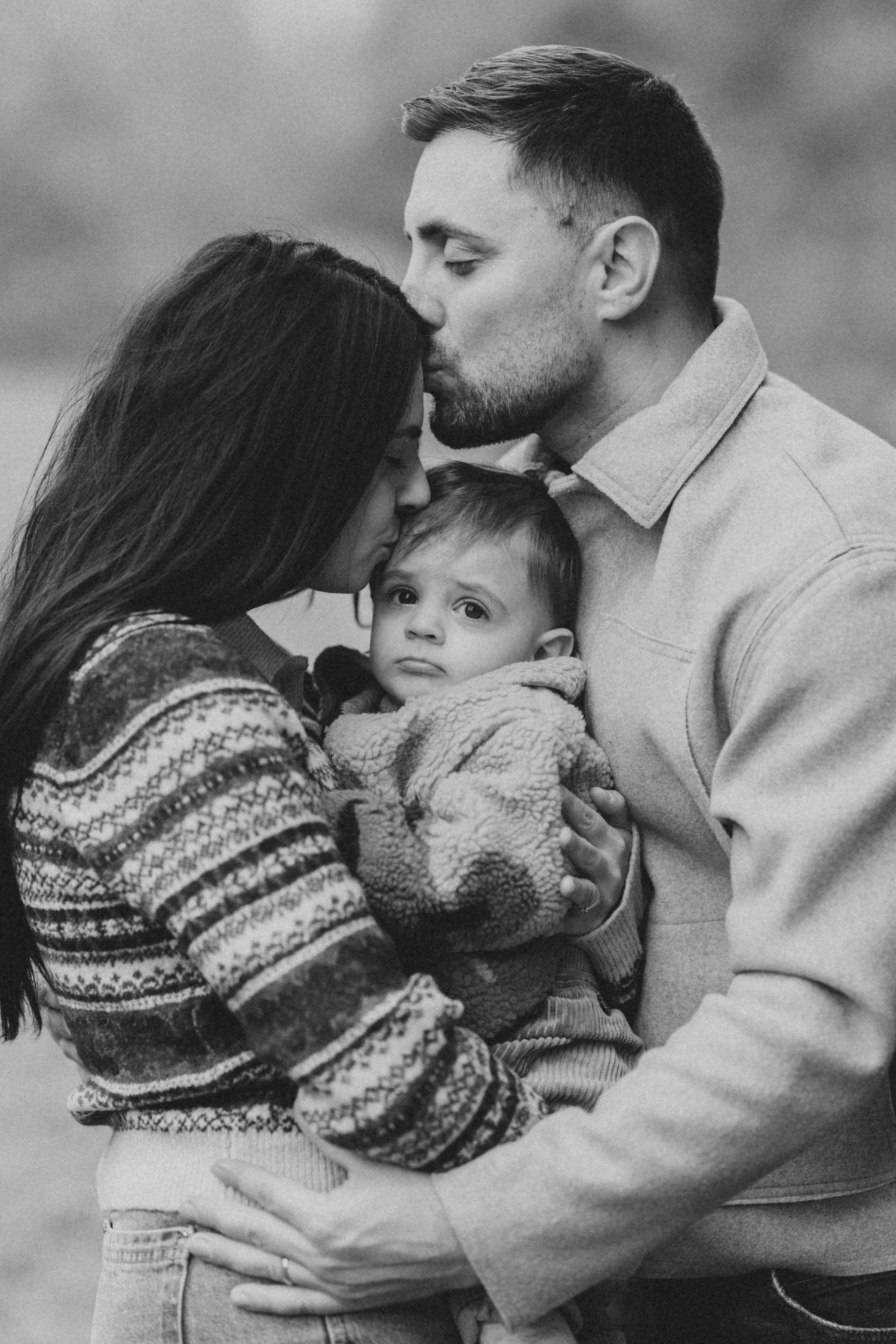 Black and white portrait of a family sharing an intimate moment together outdoors.