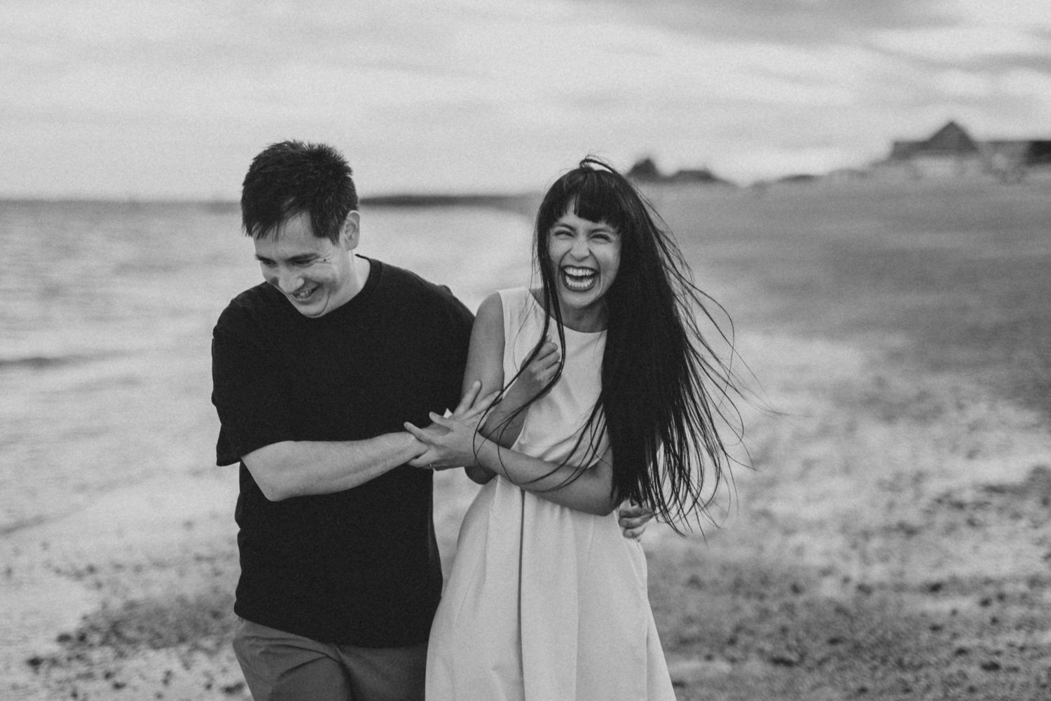 A couple shares playful moments together on a windswept beach landscape.