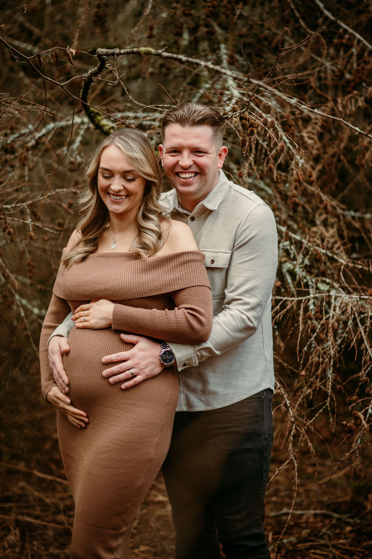 A couple embraces during a maternity photoshoot in an autumn woodland setting.