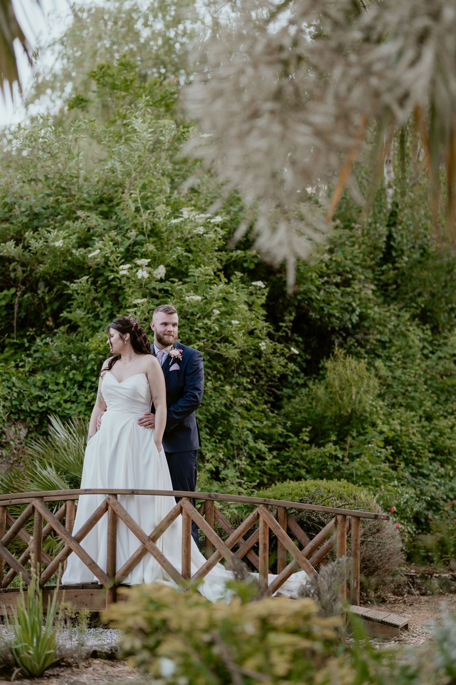 Wedding couple sharing intimate moments on a rustic wooden bridge in a garden setting.