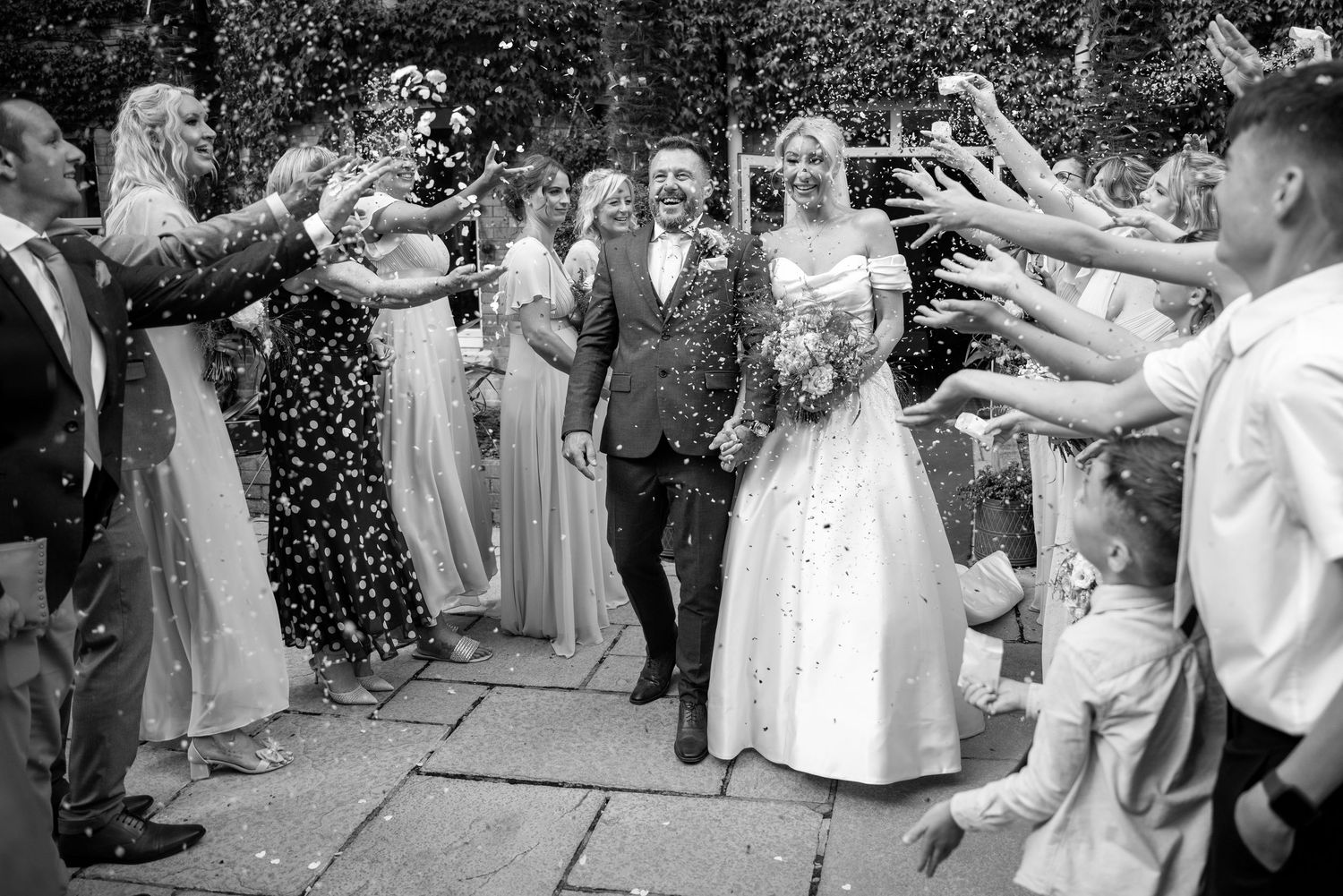 Wedding guests toss confetti during outdoor celebration.