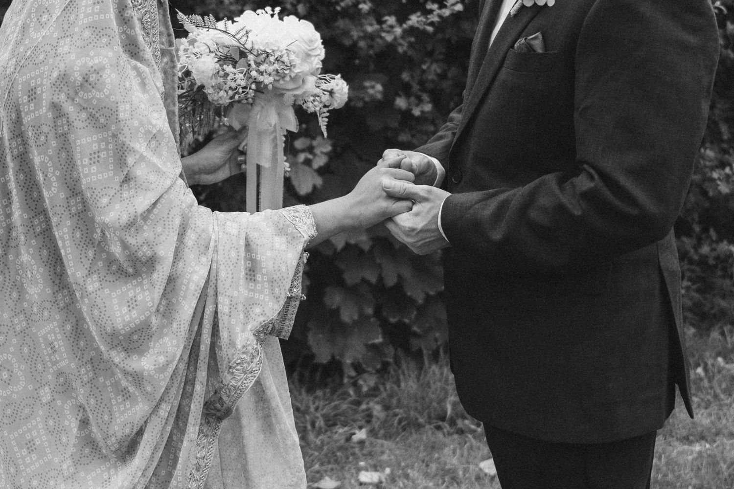 Black and white close-up of couple exchanging rings during outdoor wedding ceremony.