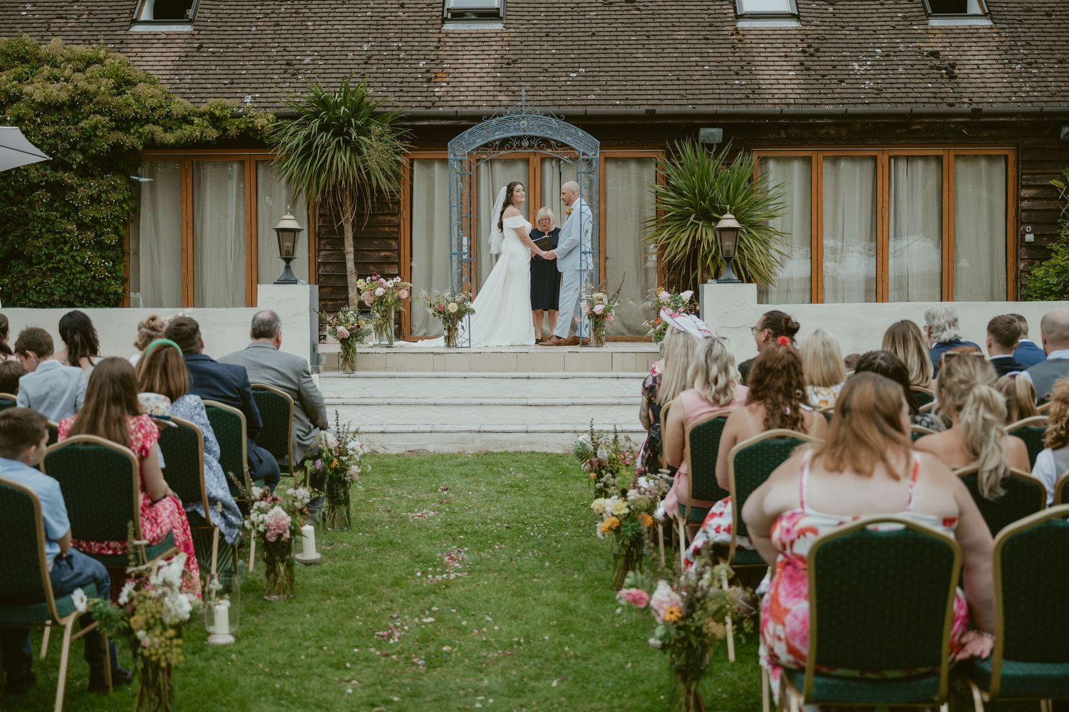 Outdoor wedding ceremony setup with rows of chairs on a green lawn facing a stone building.