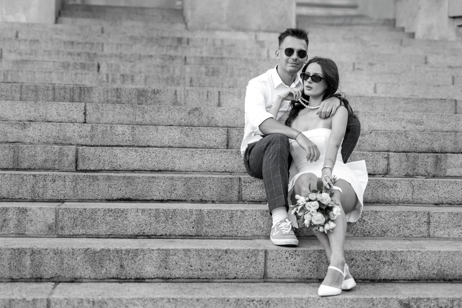 Couple sitting on stone steps in casual wedding attire.