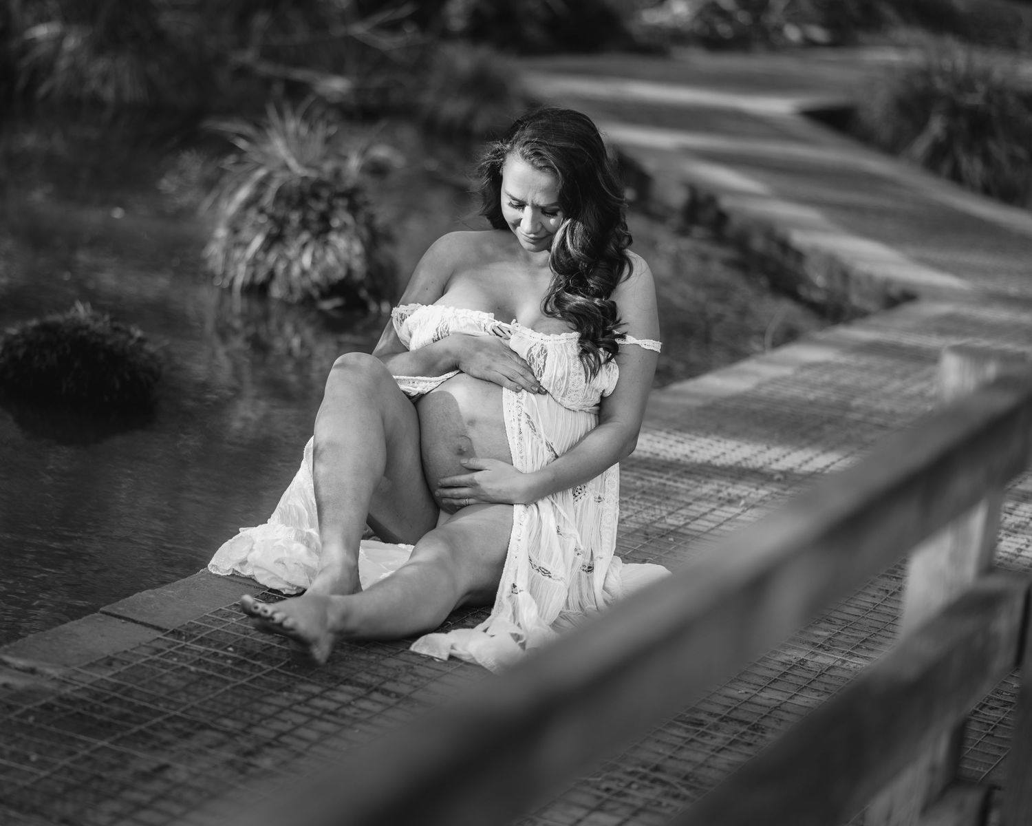 Black and white maternity portrait captured on a wooden deck with dramatic shadows.